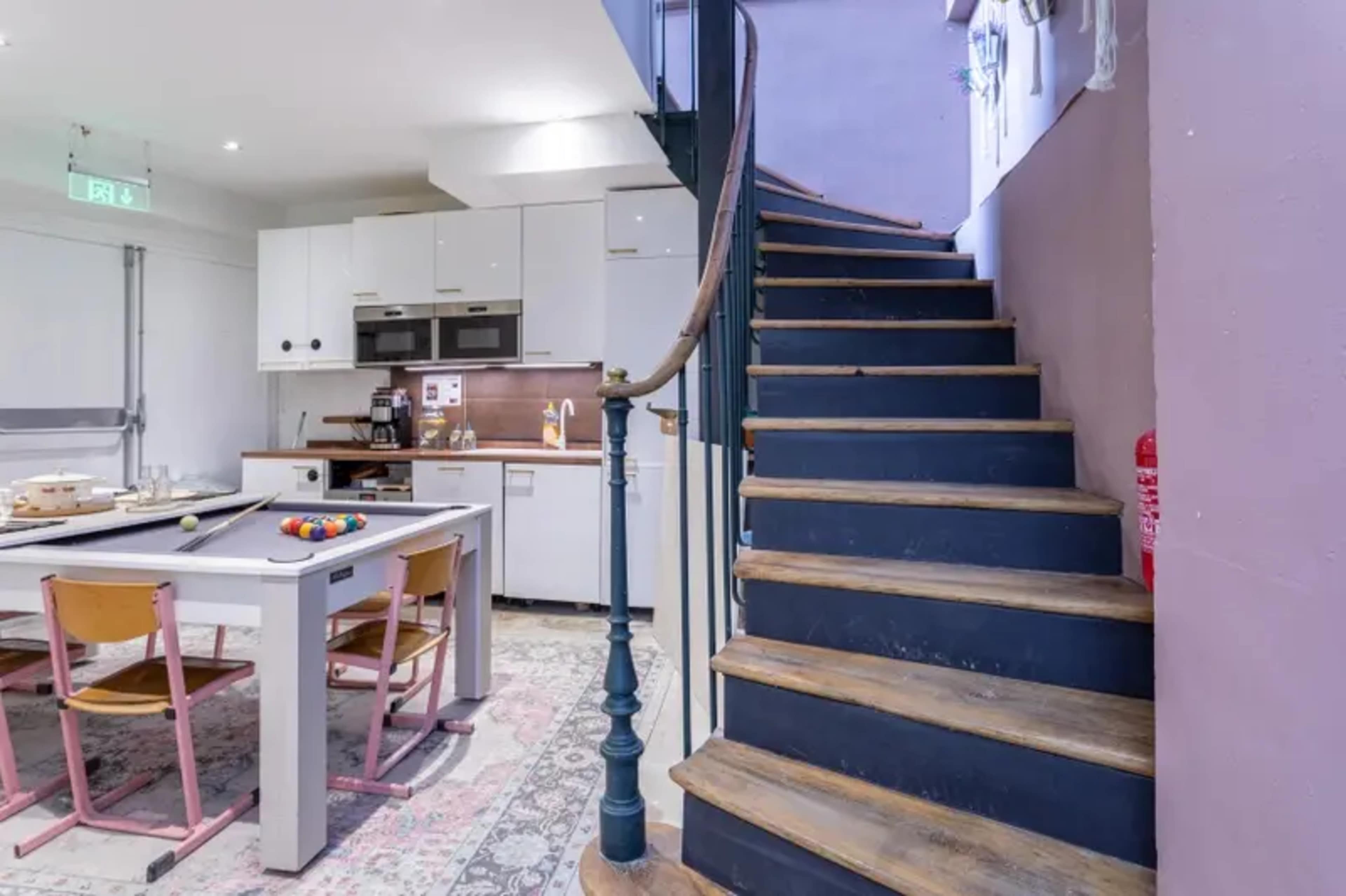 A wooden staircase with a metal banister leads to an upper floor, adjacent to a modern kitchen and dining area.