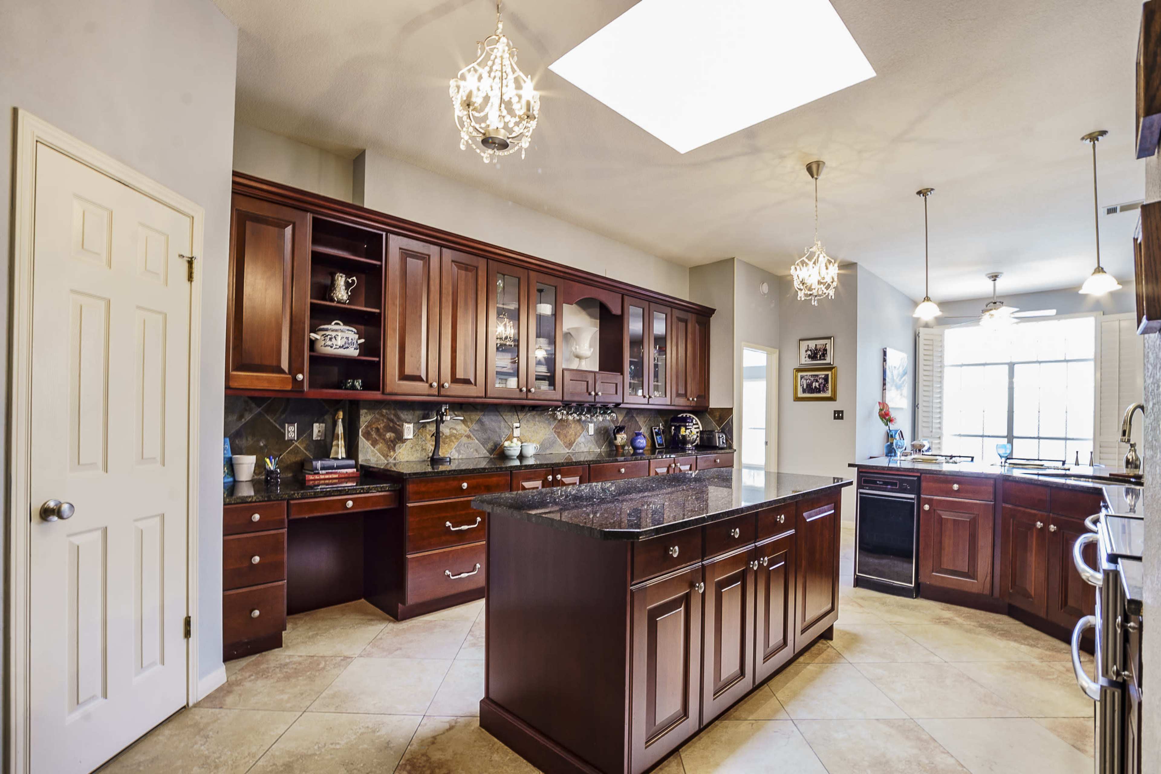 The image shows a spacious kitchen with wooden cabinetry, a large island with a granite countertop, and pendant lighting.