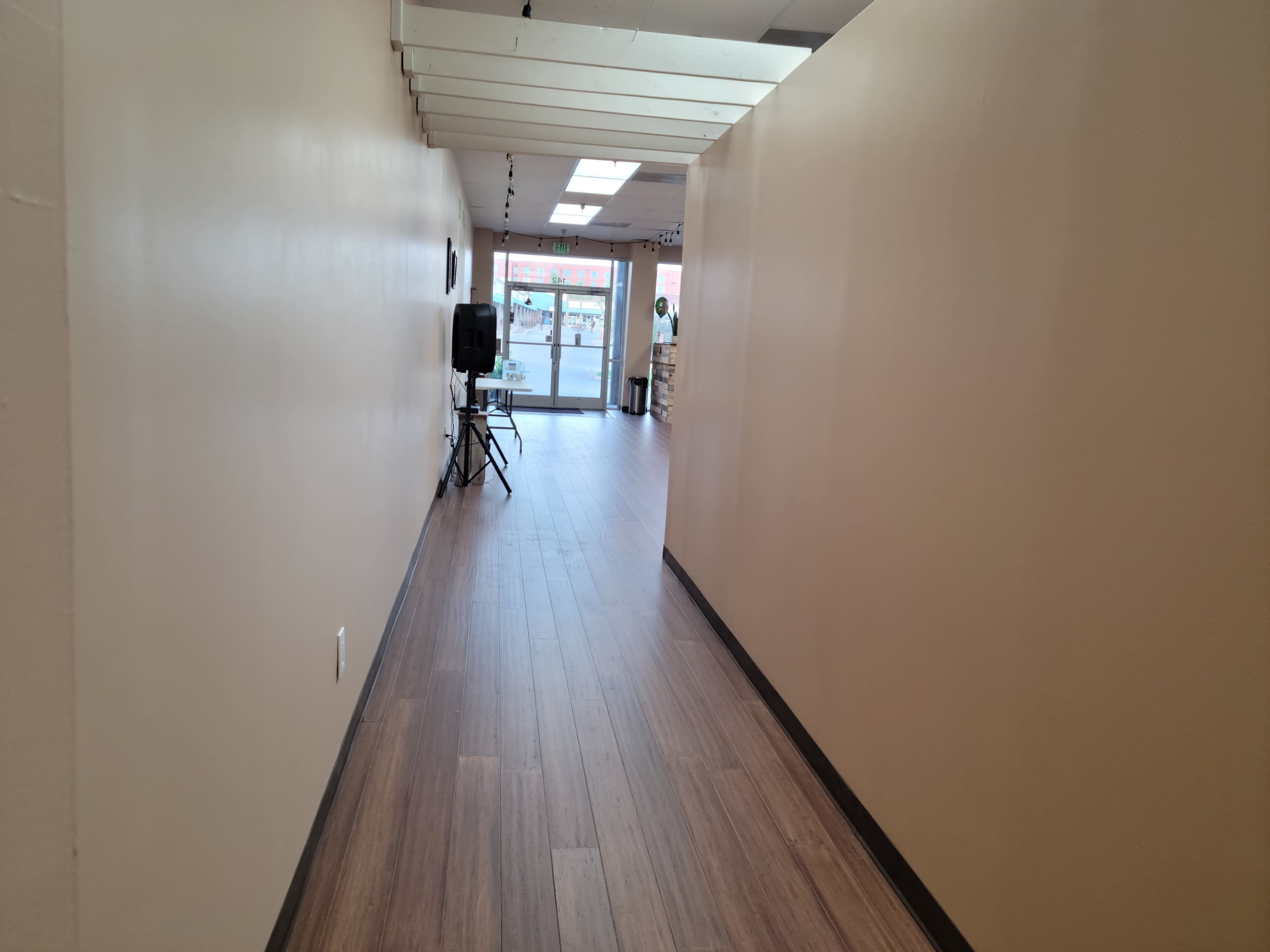 A narrow hallway with beige walls and wooden flooring leading to a glass door at the end.