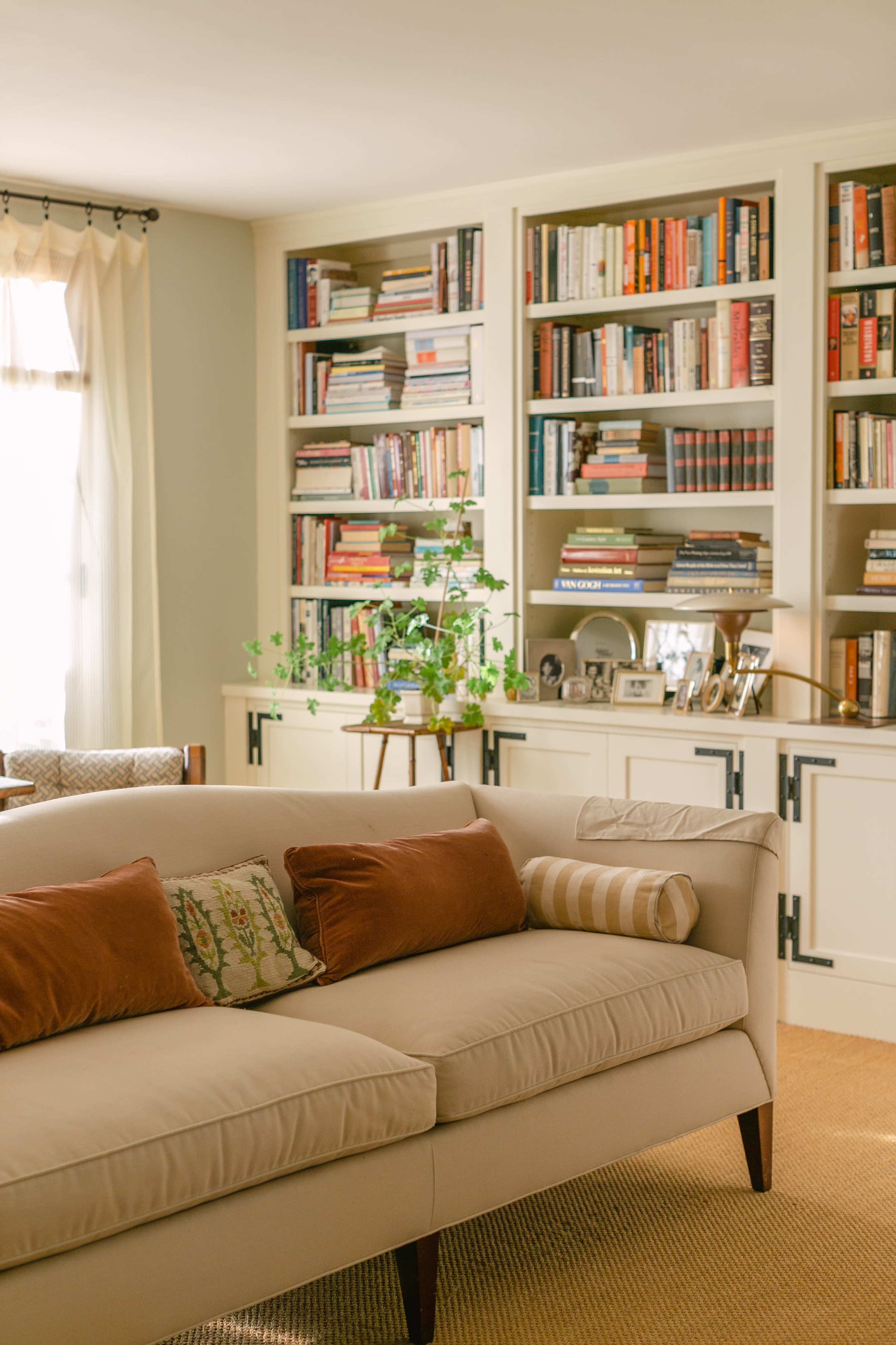 A cozy living room features a beige sofa with throw pillows, positioned in front of built-in shelving filled with books and decorative items.