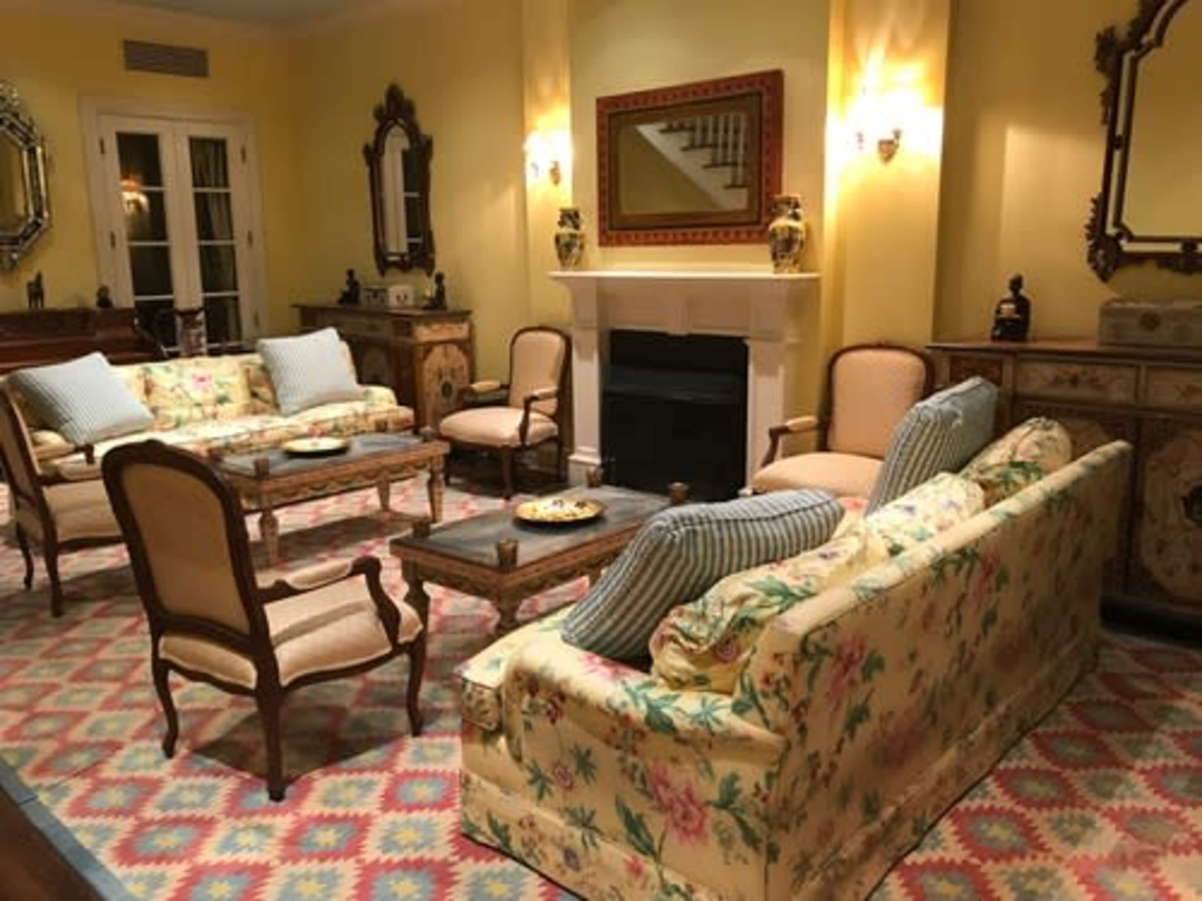 A cozy living room with floral-patterned sofas, armchairs, a coffee table, and a fireplace, all arranged around a colorful rug.