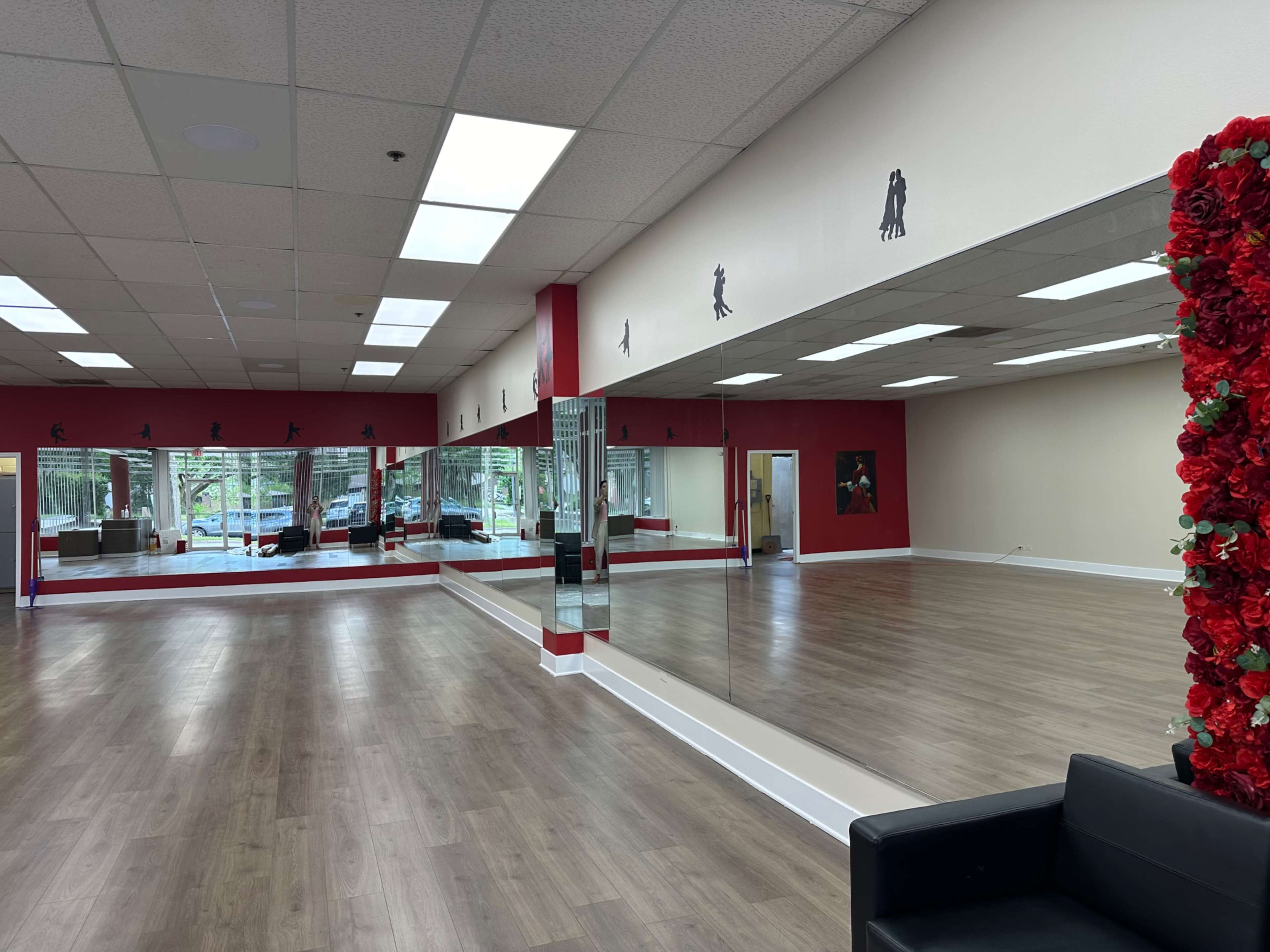 A spacious dance studio with large mirrors, wooden flooring, and a decorative wall featuring silhouettes of dancers.