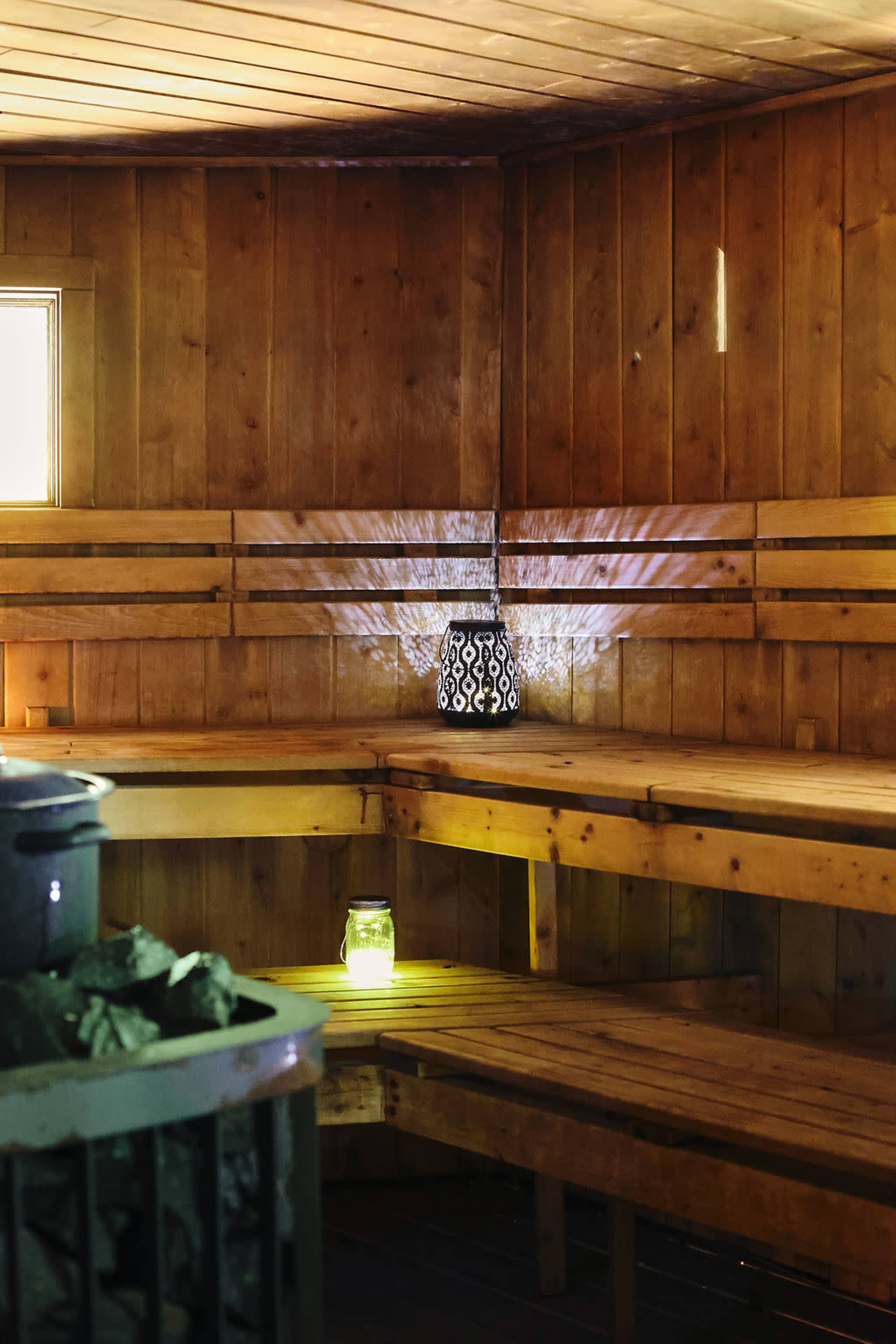 The image shows the interior of a wooden sauna with benches, a lantern casting light, and jars placed on the benches.