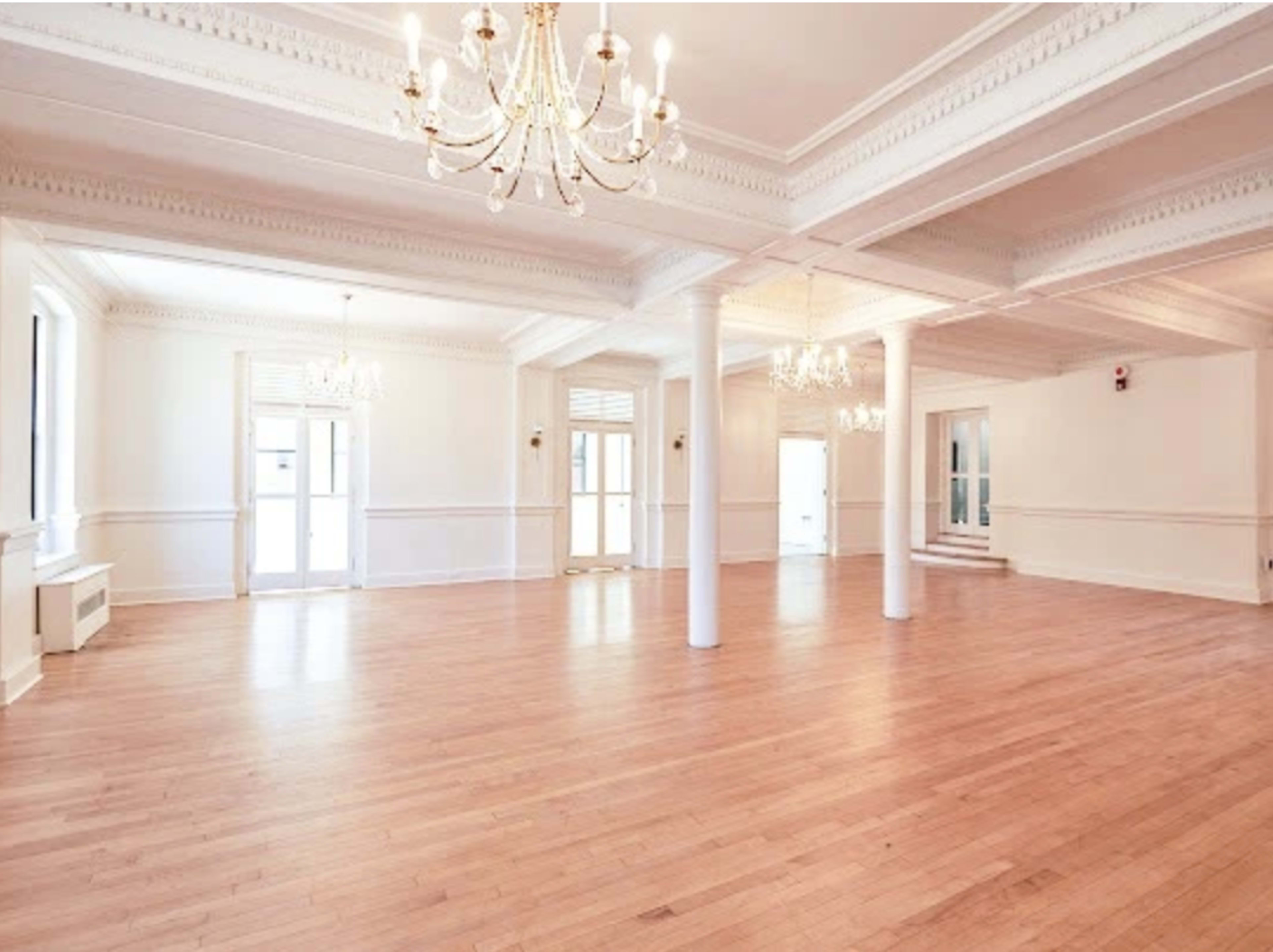 A spacious, well-lit interior room with wooden floors and multiple chandeliers.