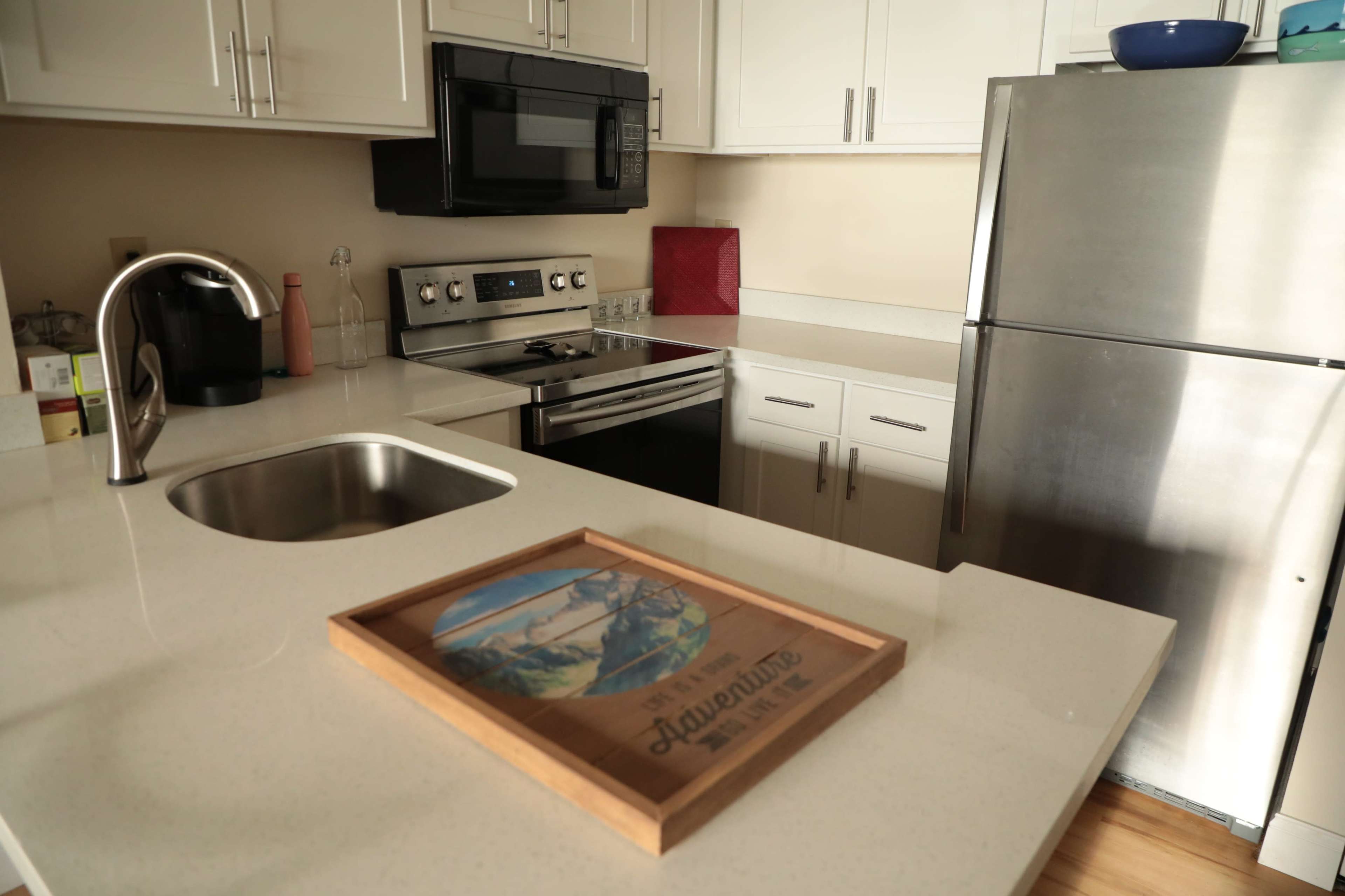 A modern kitchen features white cabinetry, stainless steel appliances, and a wooden tray with a landscape illustration on the countertop.