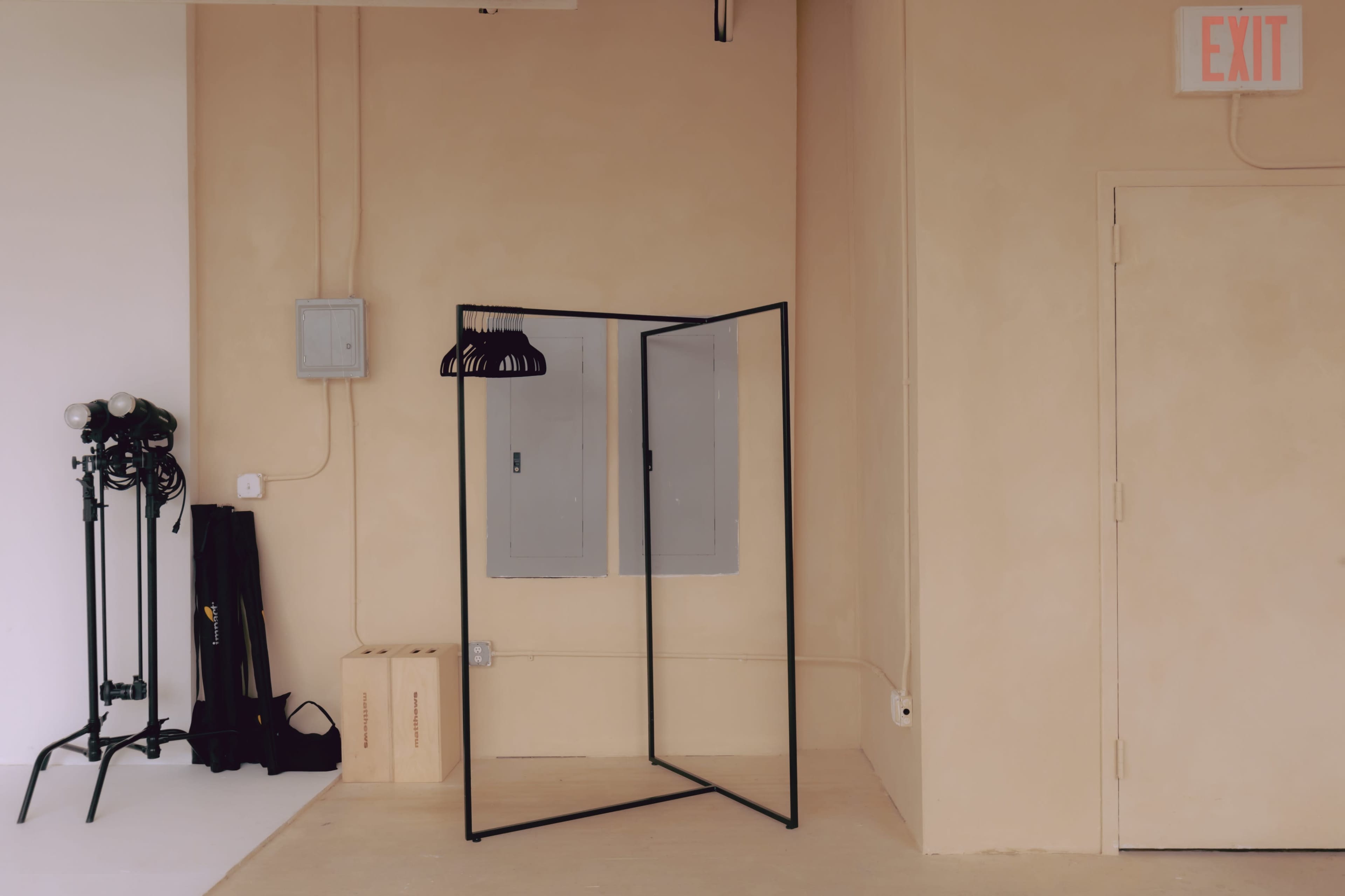 A minimal interior space featuring a black clothing rack, a beige wall, electrical panels, and an exit sign.