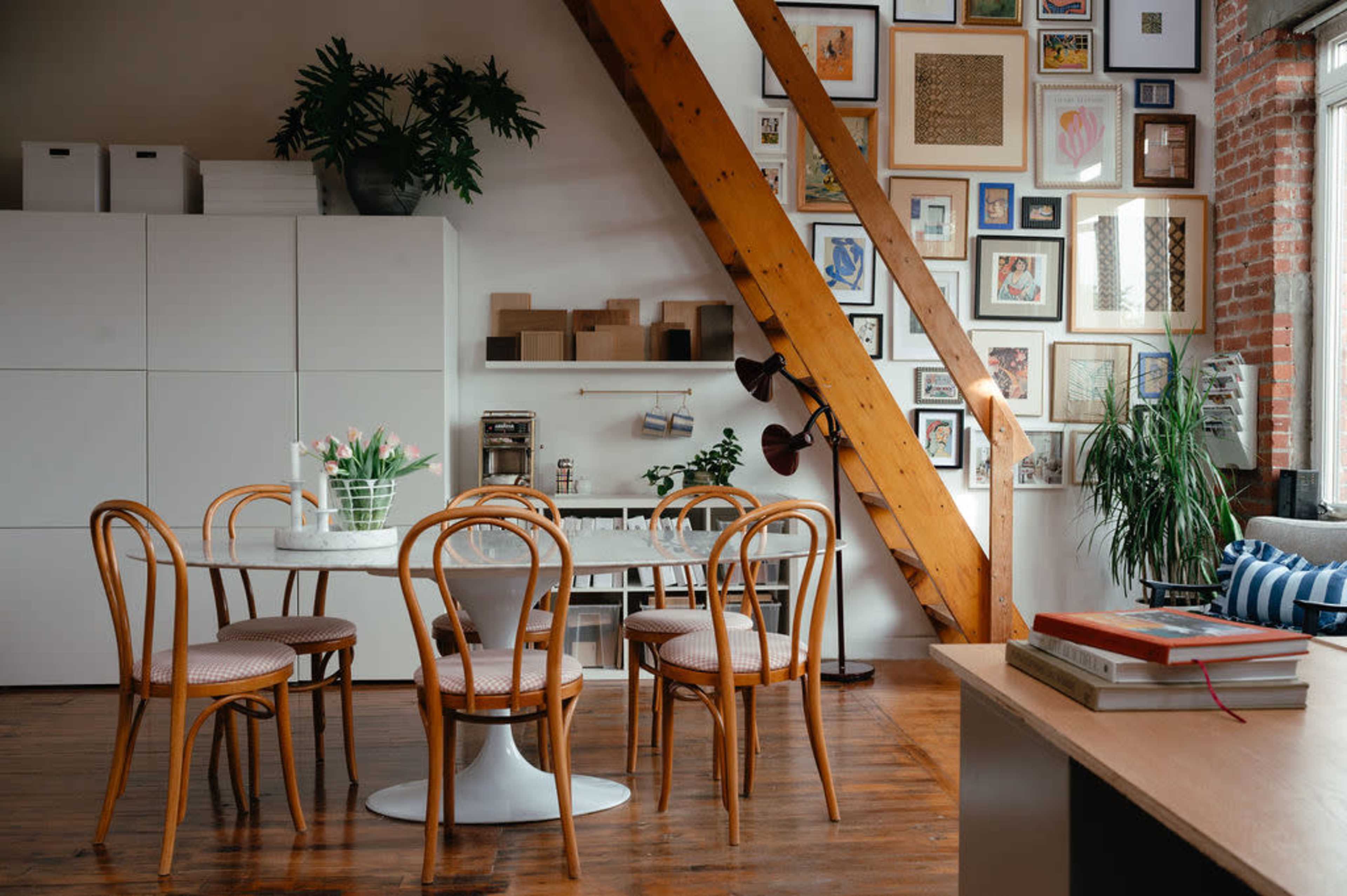 A dining area with a round white table surrounded by wooden chairs, set against a wall adorned with various framed artworks and a wooden beam ceiling.