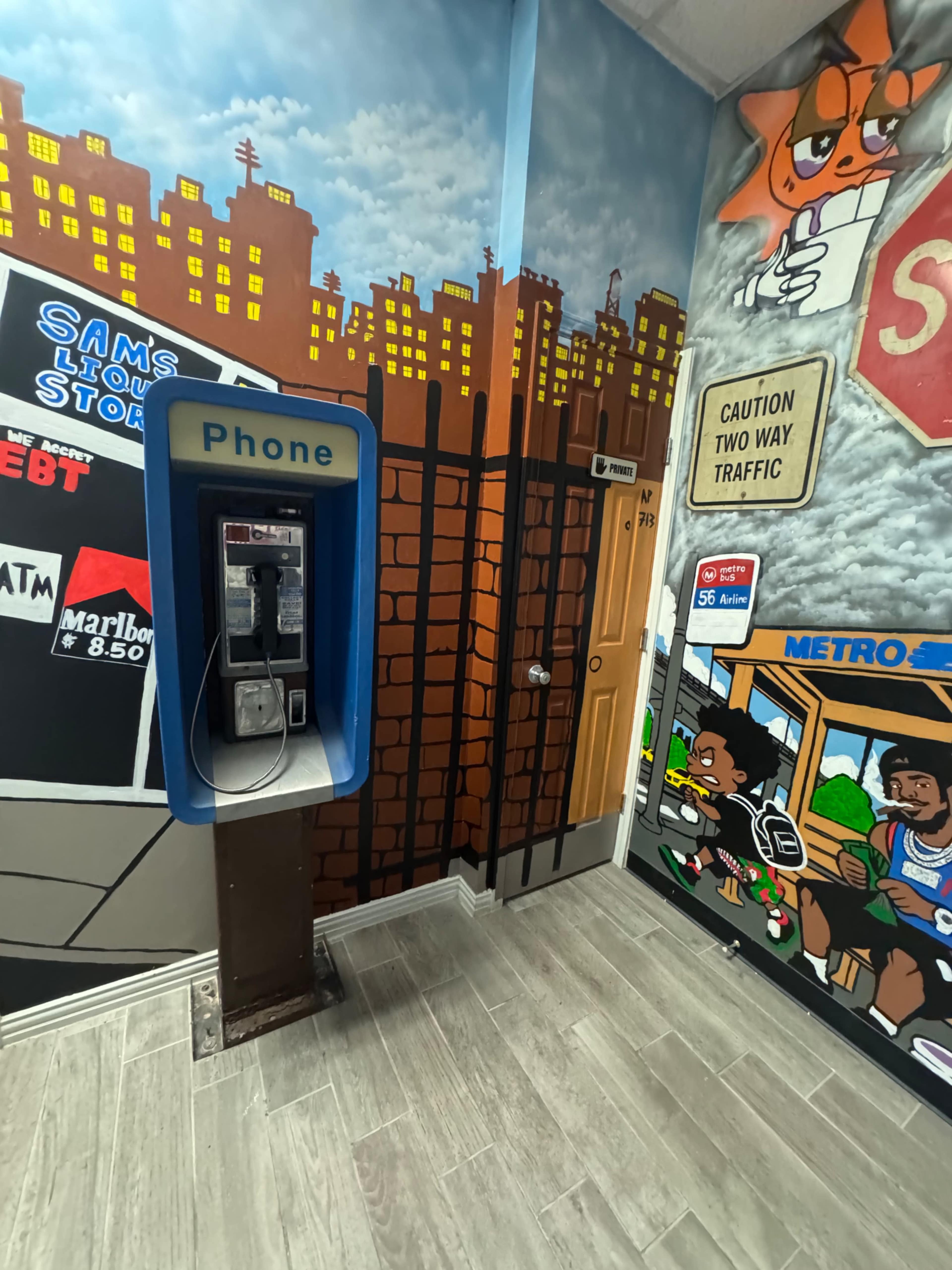 The image shows a payphone in a corner of a room adorned with colorful murals depicting urban scenes and traffic signs.