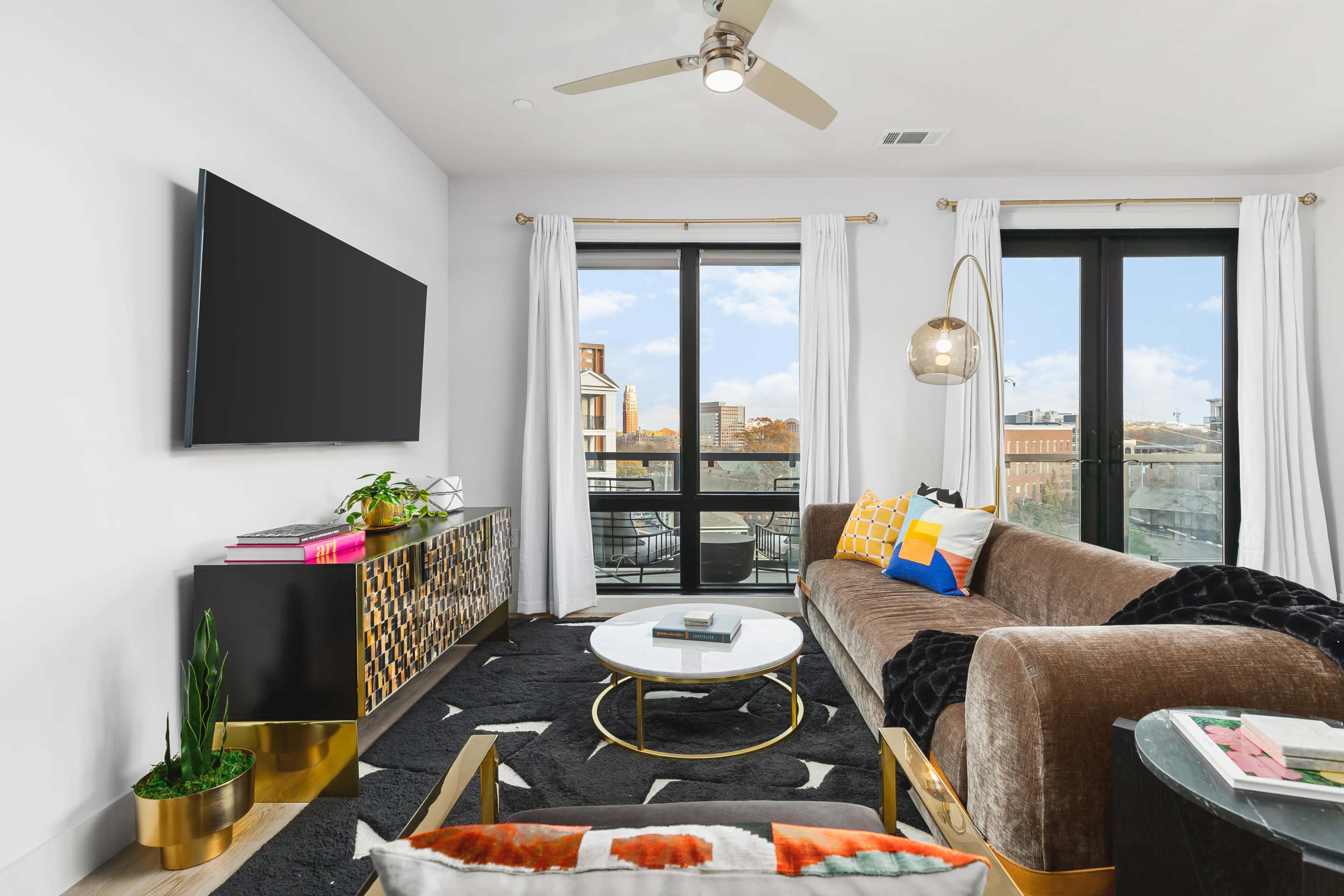The living room features a sofa, a round coffee table, and a large window with views of an outdoor balcony.