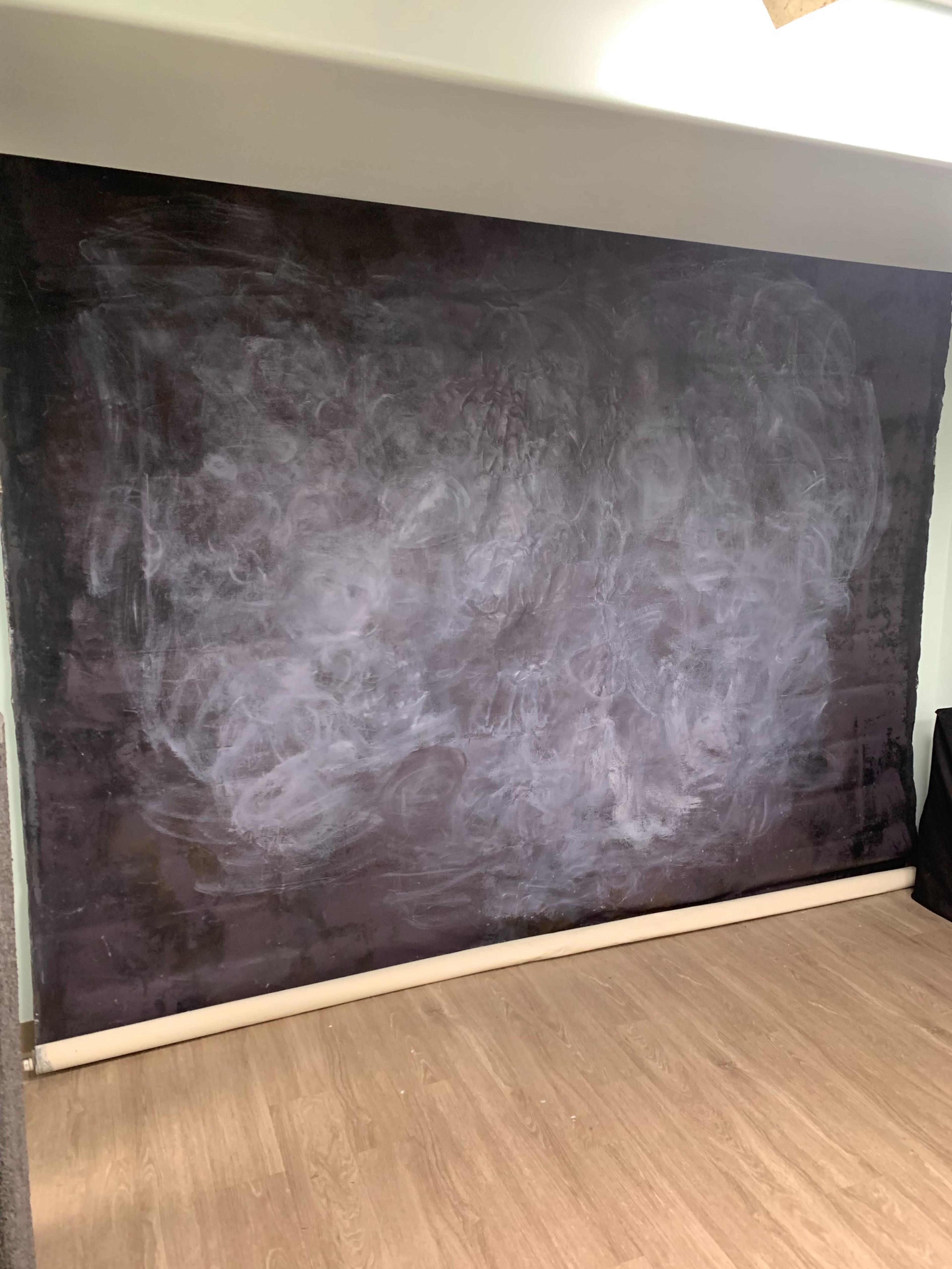 A large blank wall with a dark surface and a rolled-up edge is visible in a room with wooden flooring.