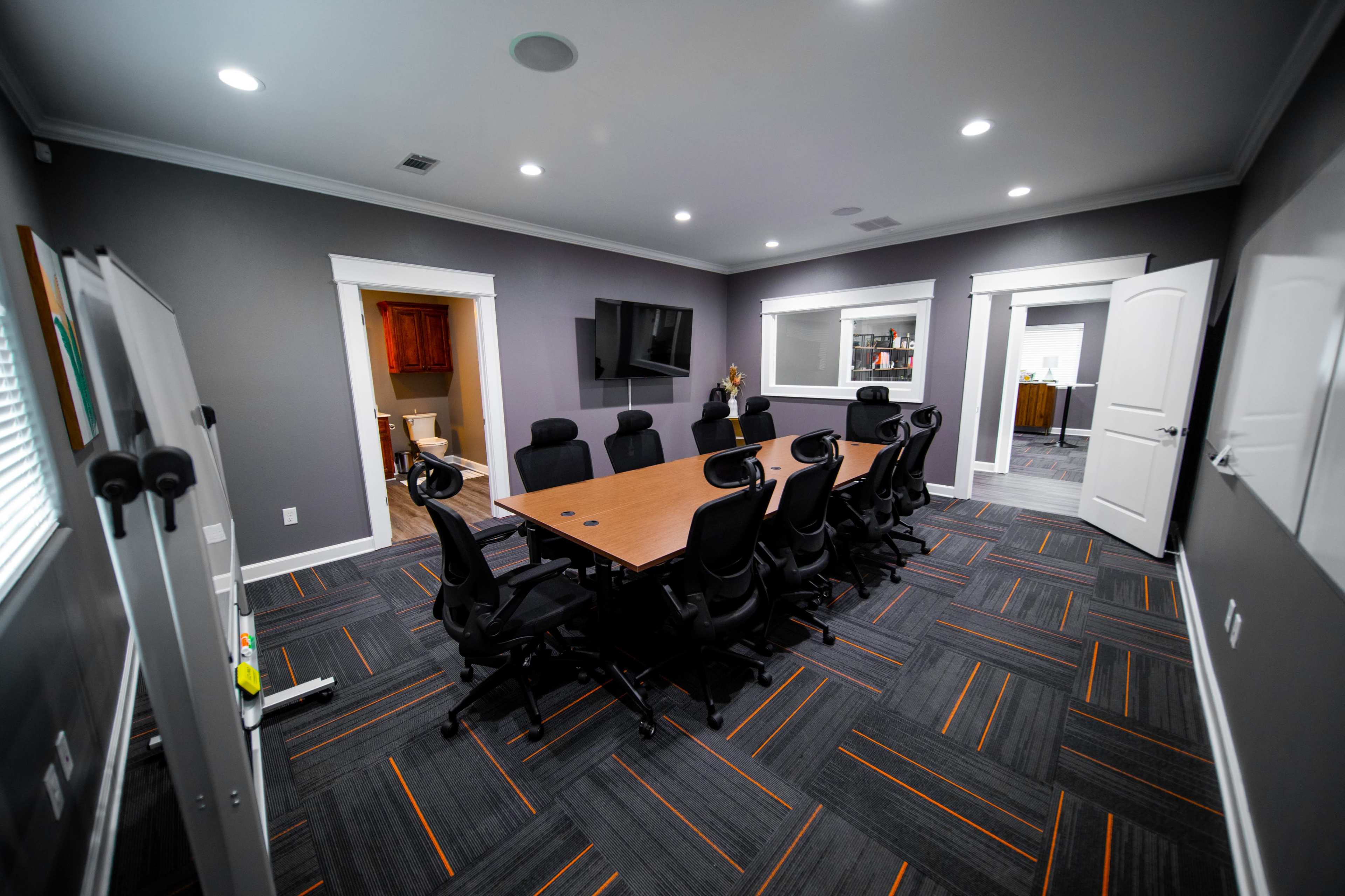 A modern conference room with a large rectangular table surrounded by black office chairs and features two doorways leading to other rooms.