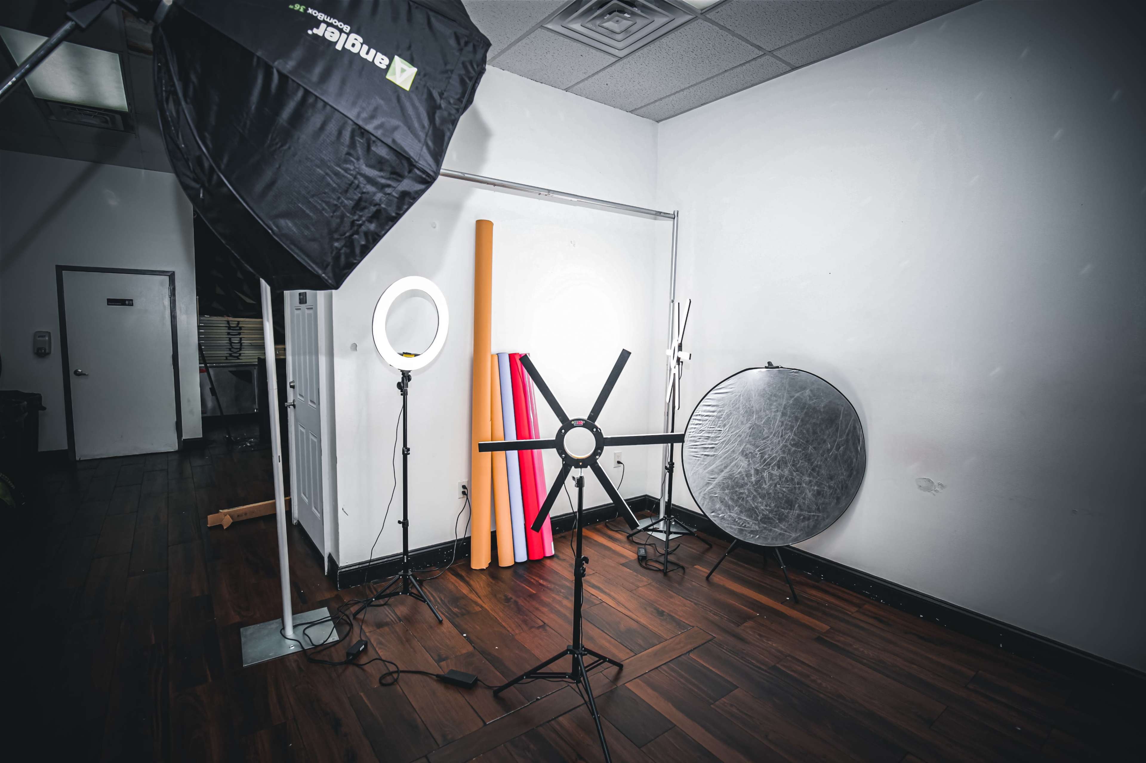 The image shows a photography studio setup with various lighting equipment and backdrops arranged against a white wall.