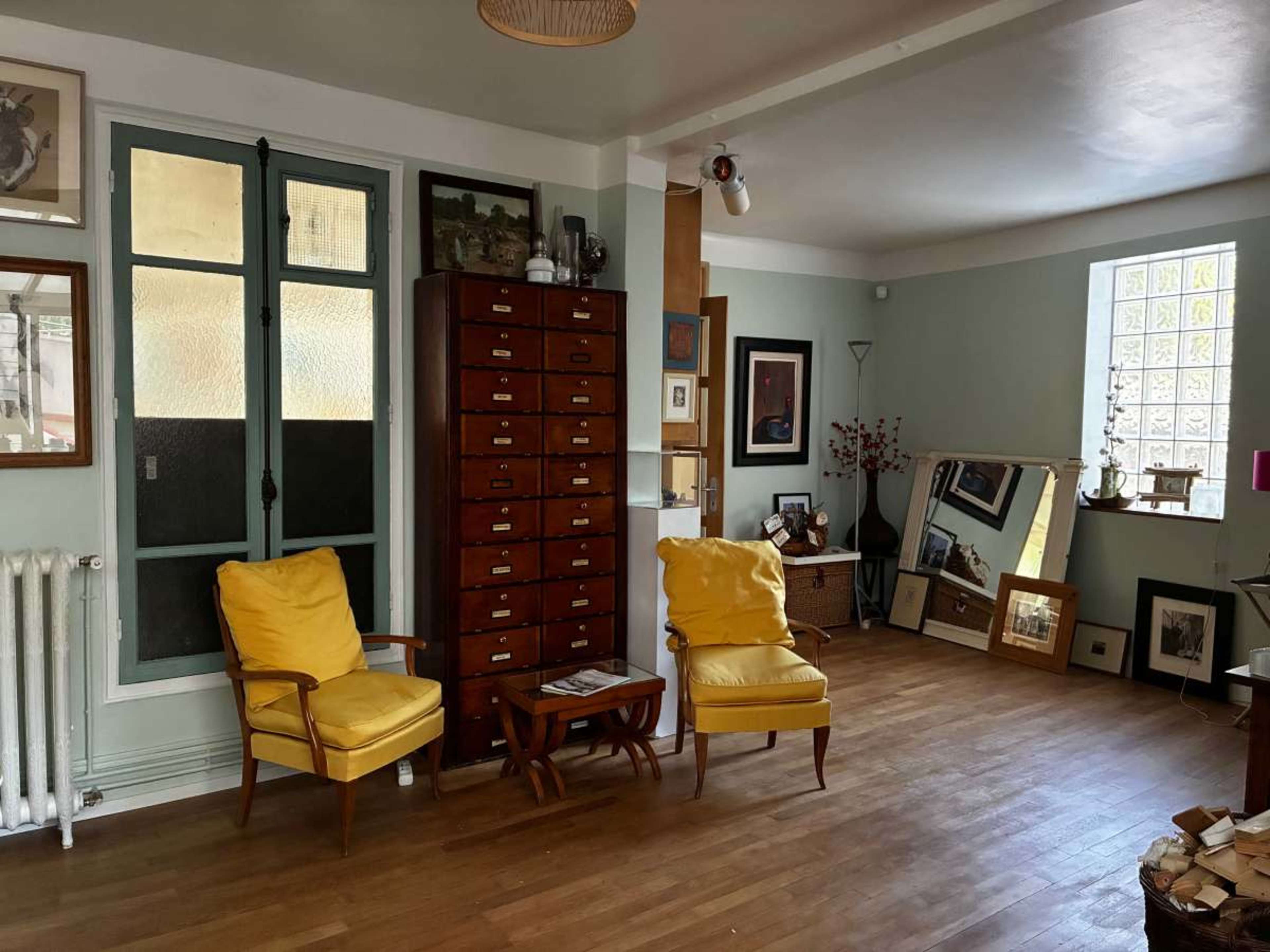 The room features two yellow armchairs, a wooden chest of drawers, framed artwork on the walls, and a large mirror reflecting part of the space.