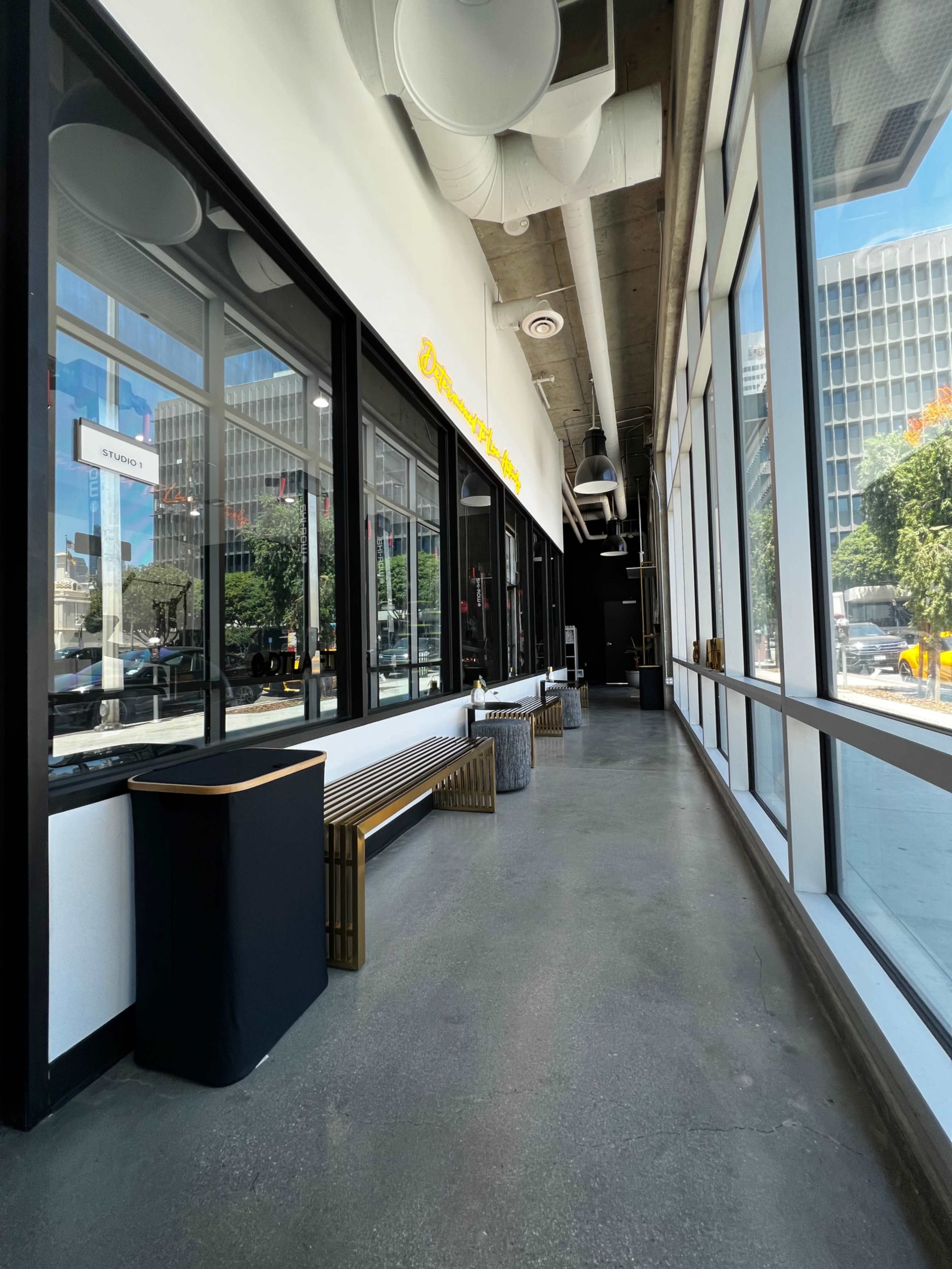 A long, modern hallway with large windows along one side, featuring benches and contemporary furniture.