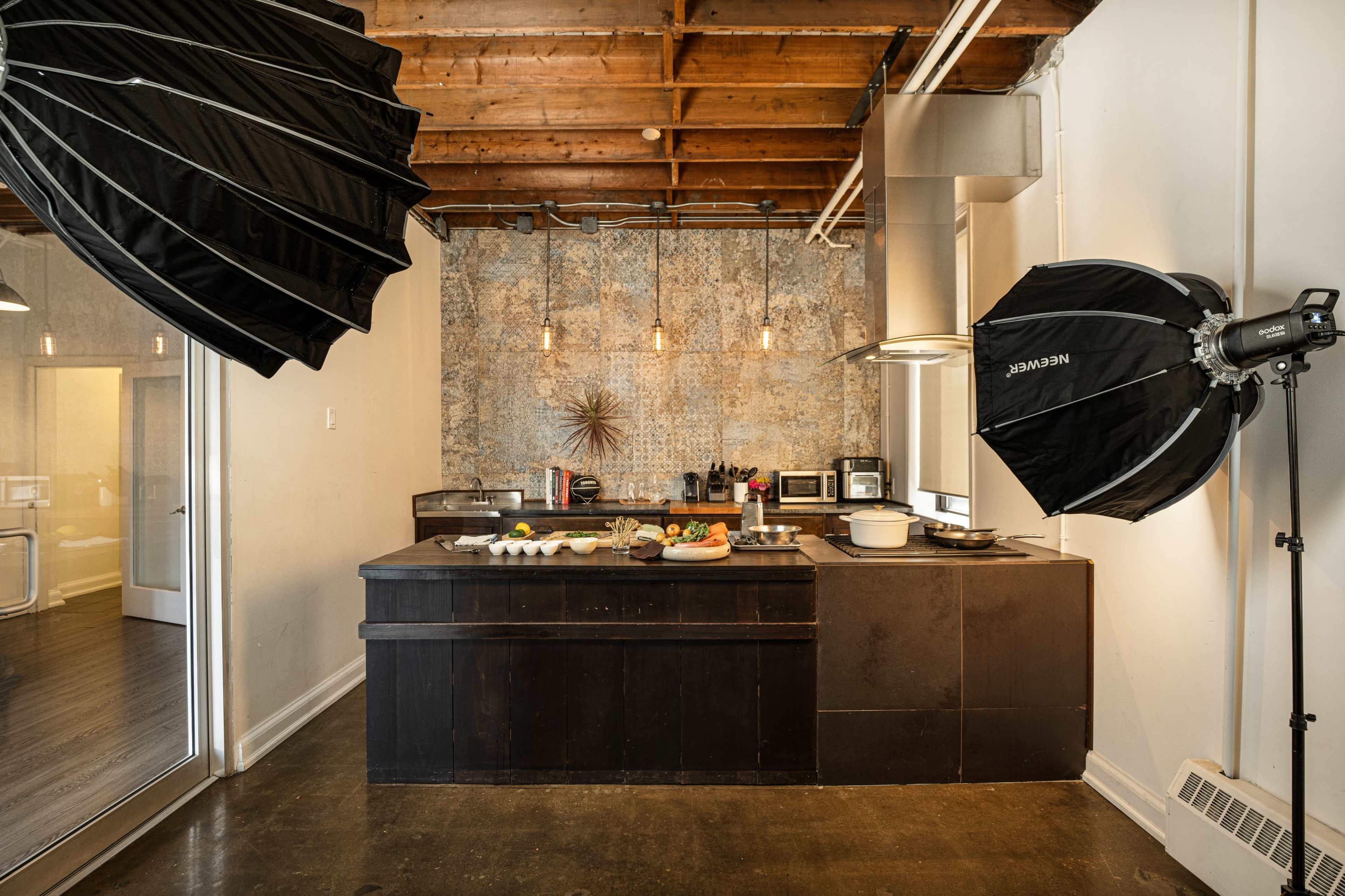 The image shows a kitchen area with a wooden counter, various kitchen appliances, and photography lighting equipment set up nearby.