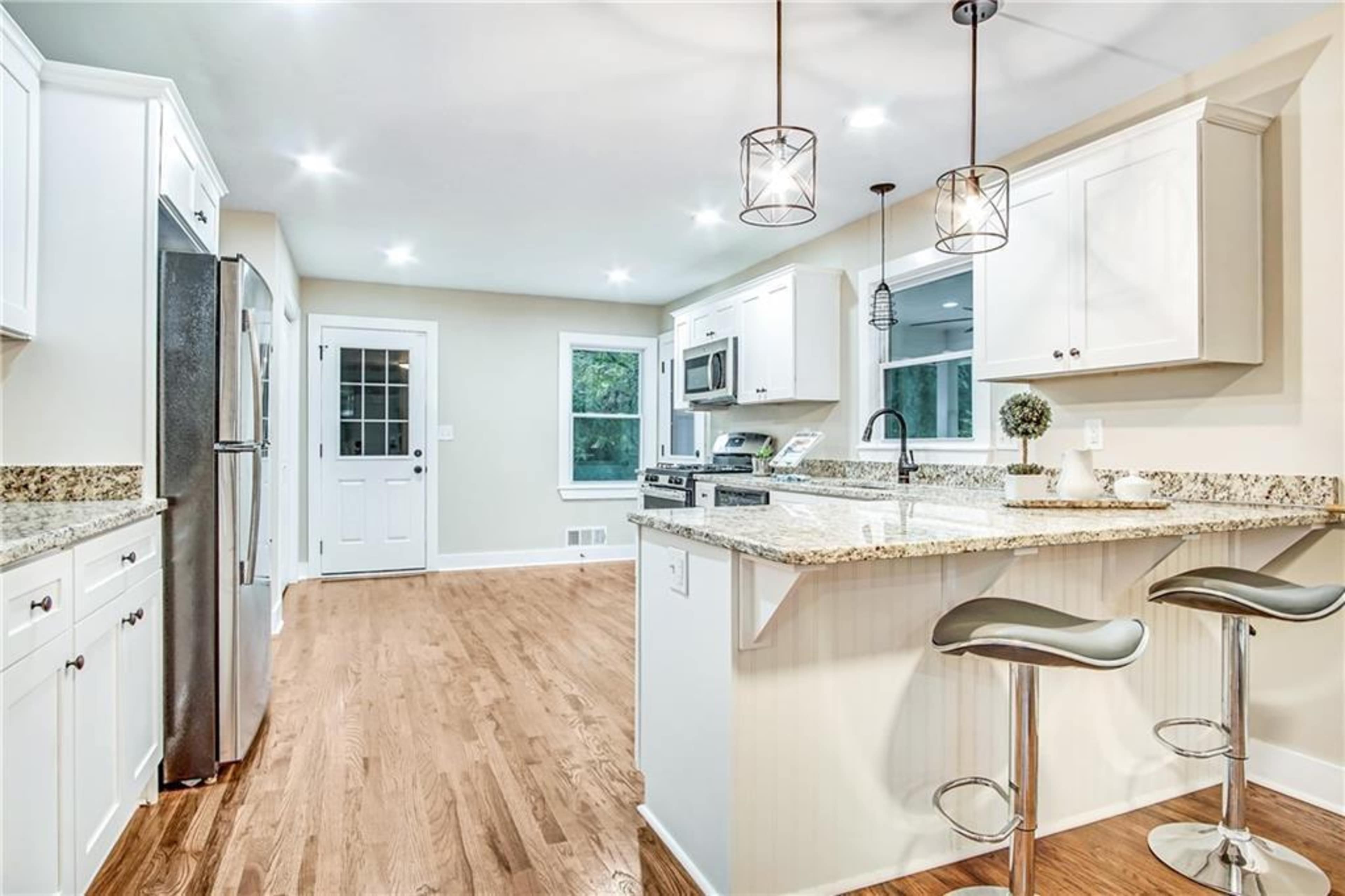 A modern kitchen with white cabinetry, granite countertops, stainless steel appliances, and a breakfast bar with two stools.