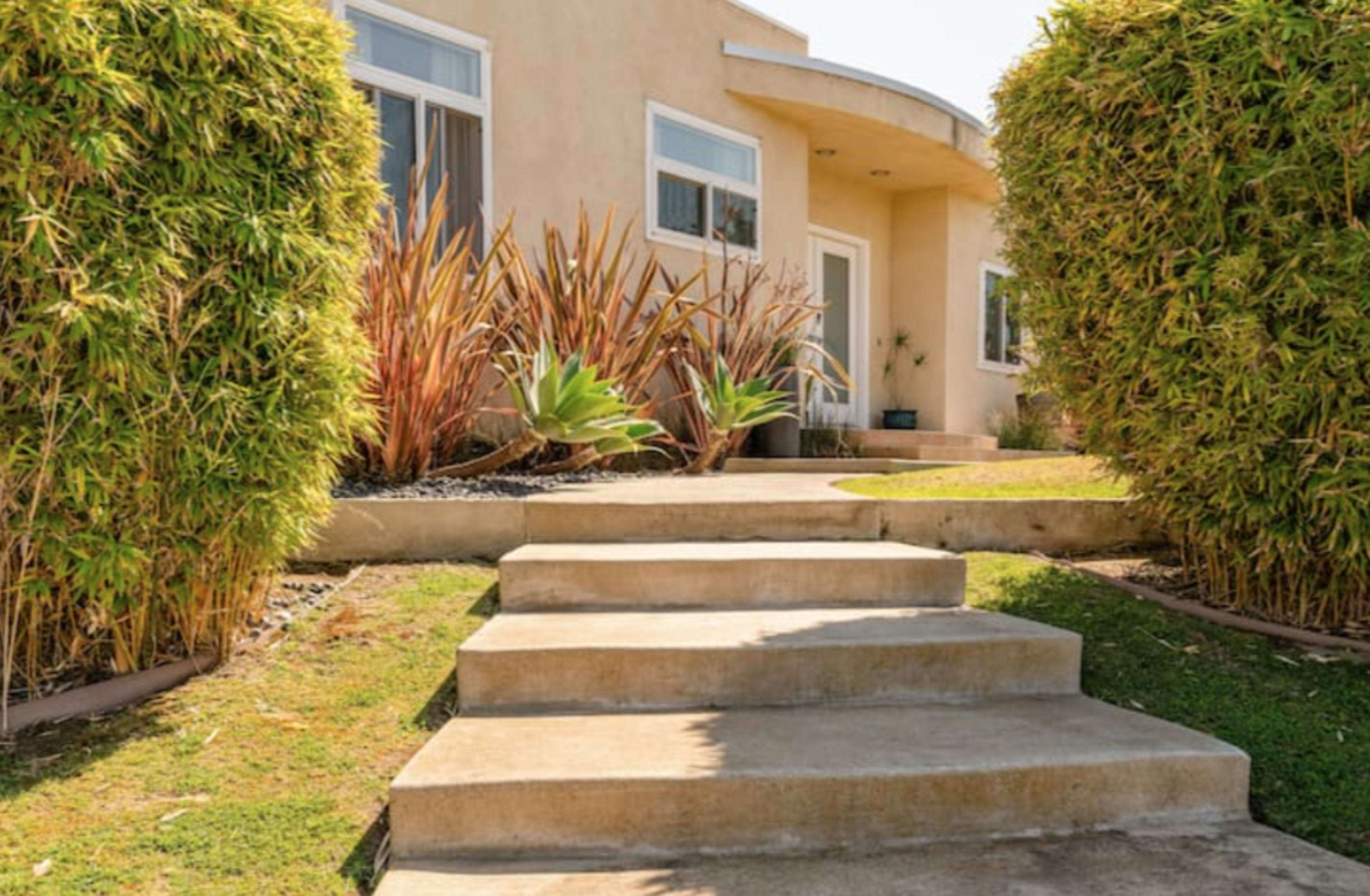 A set of stone steps leads to a modern house surrounded by trimmed hedges and decorative plants.