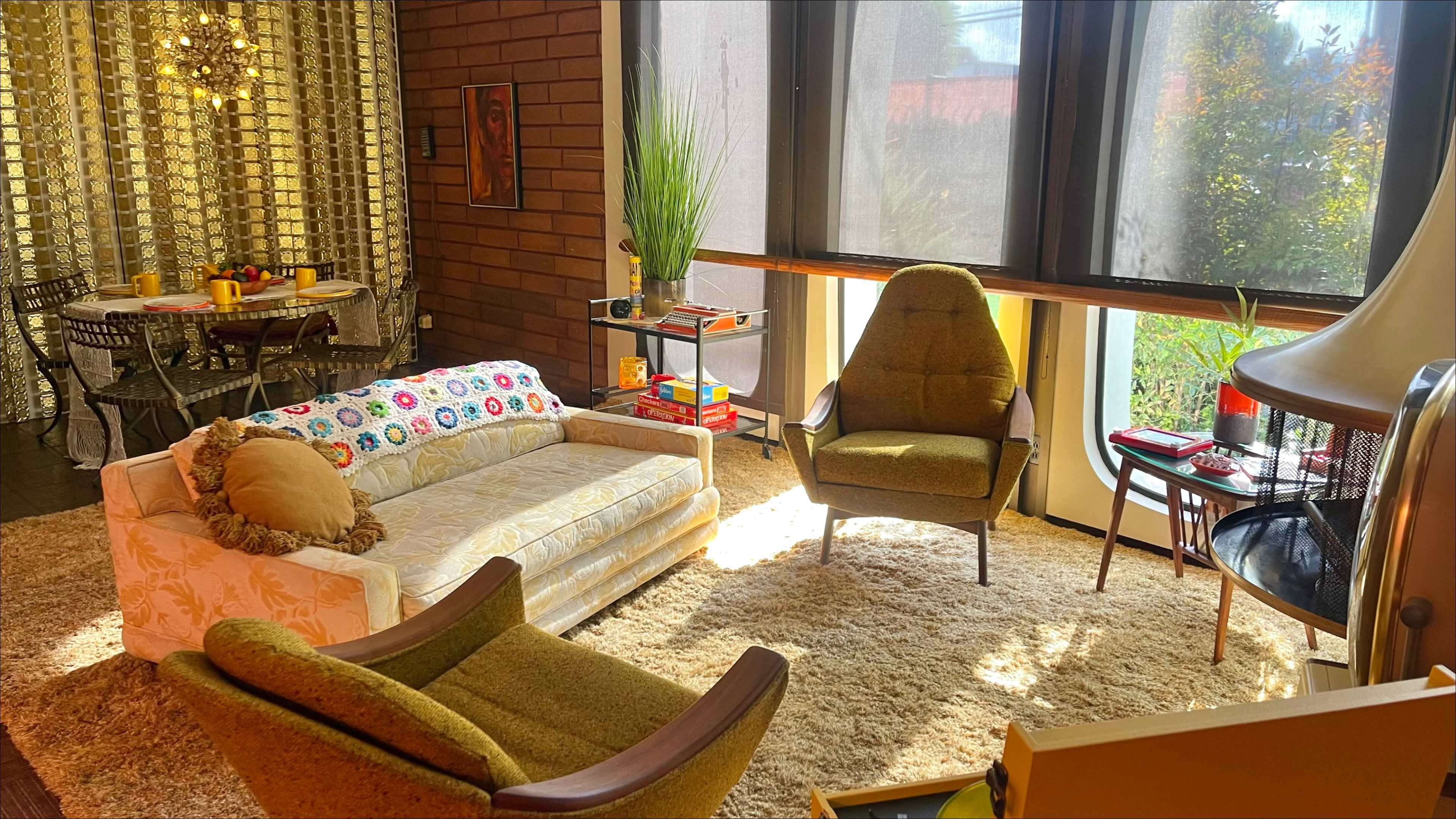 The image shows a cozy living room featuring a vintage sofa, two armchairs, a coffee table, and large windows allowing natural light to fill the space.
