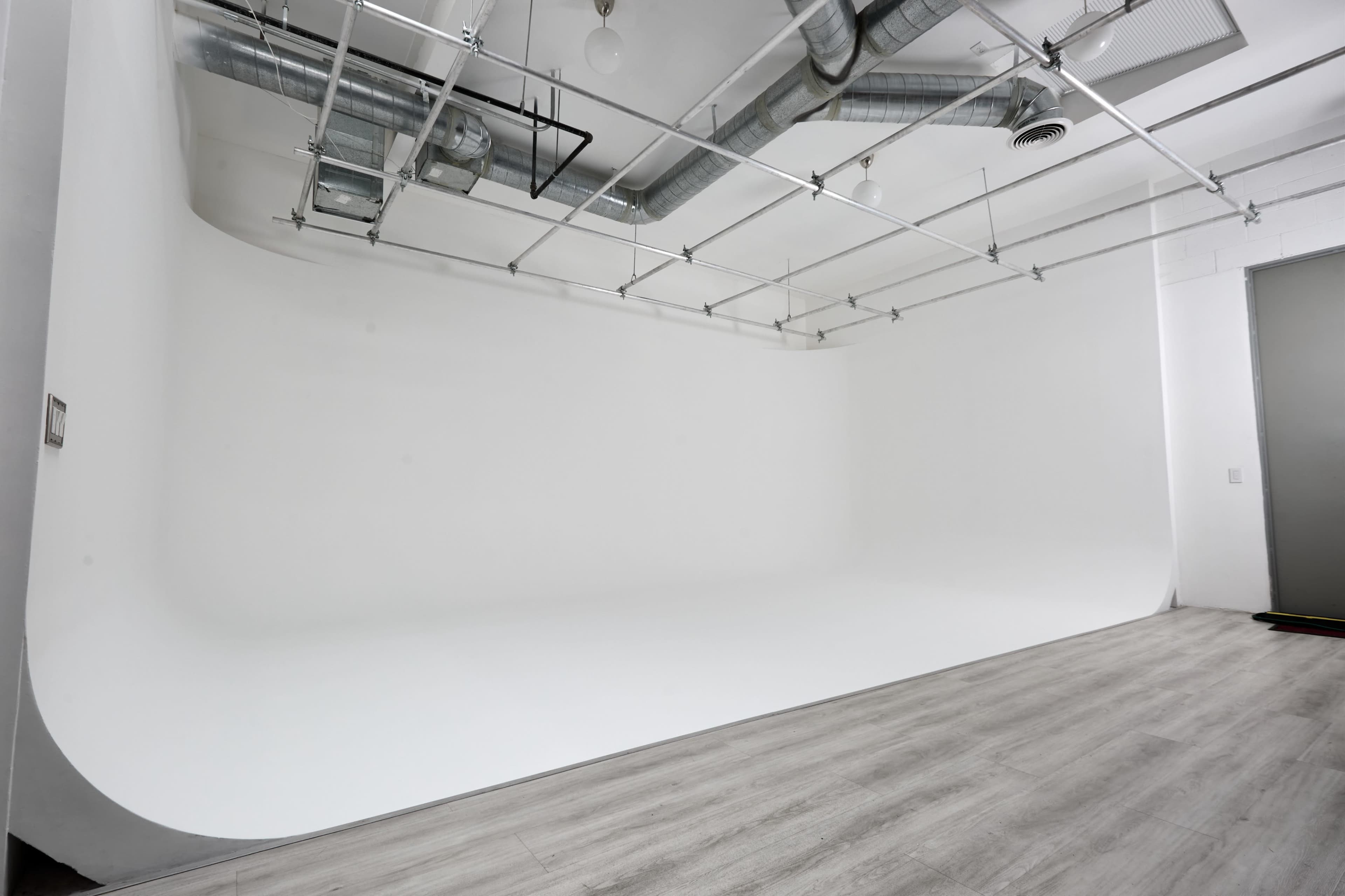 The image shows a spacious photography studio with a seamless white backdrop and wooden flooring.