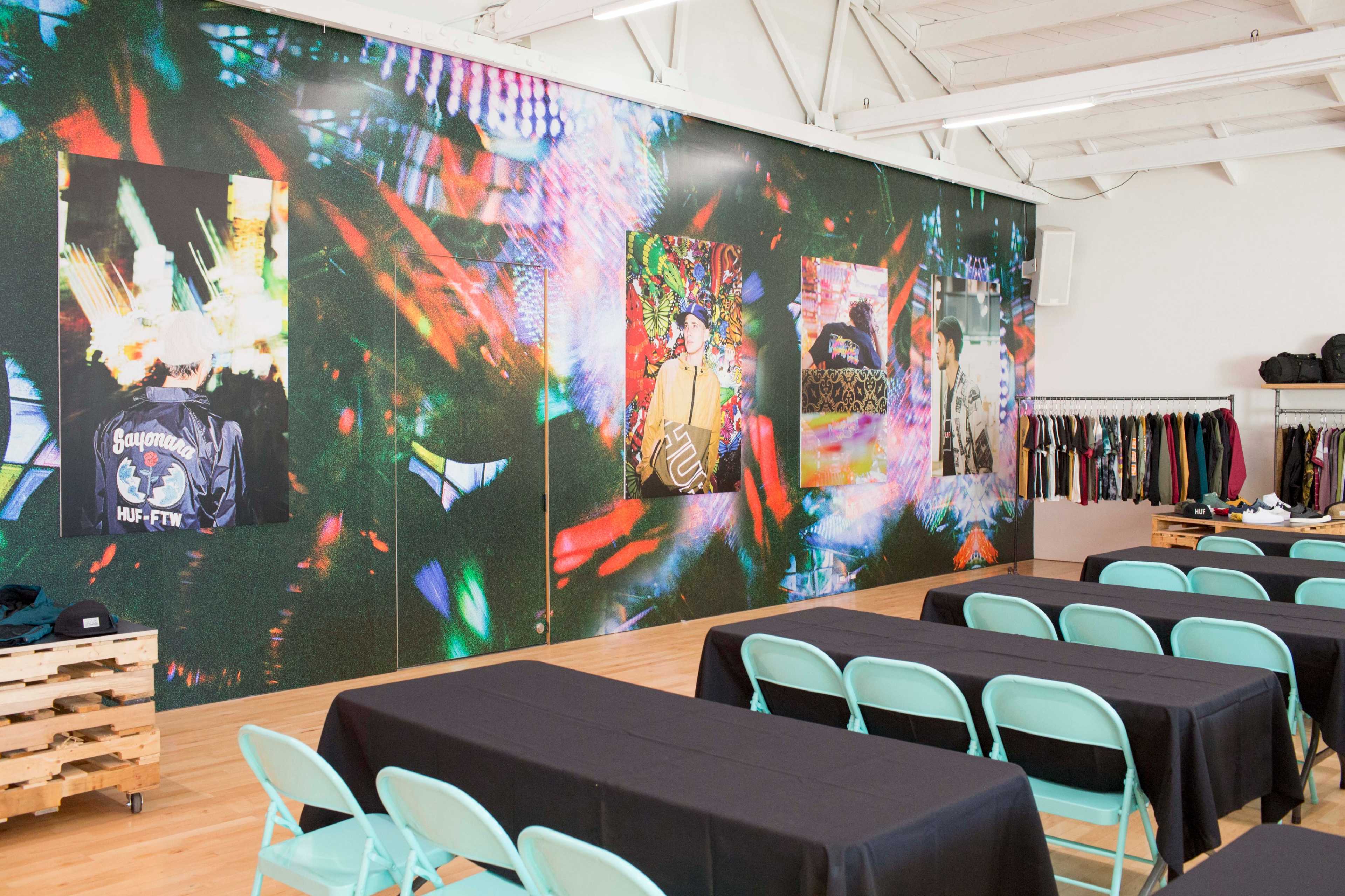 A spacious room with a vibrant wall adorned with large, colorful artworks and a set of tables arranged with turquoise chairs in front.