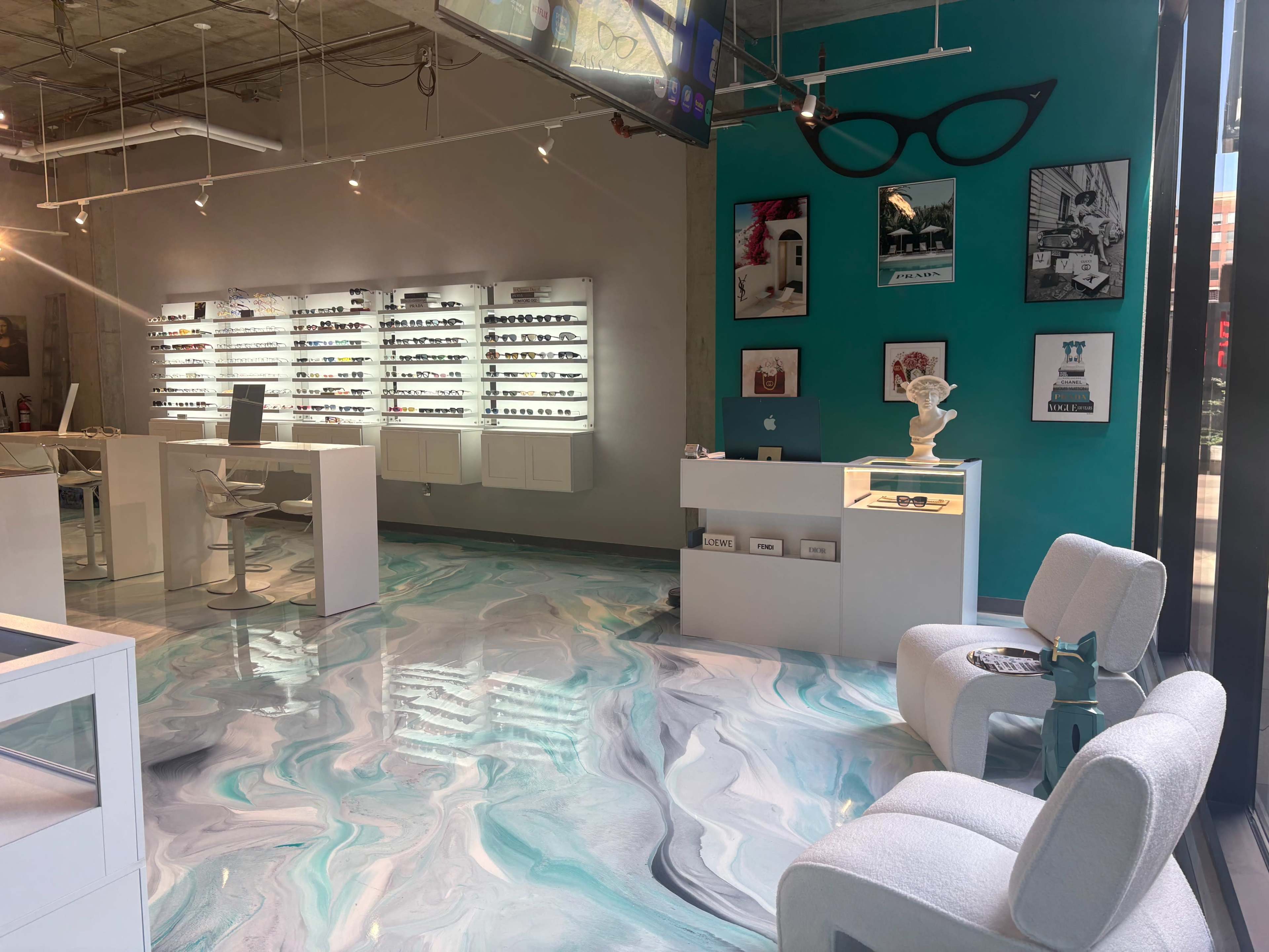 The image shows a modern optical shop featuring sleek display shelves for glasses, a stylish chair area, and a vibrant turquoise accent wall adorned with framed art.