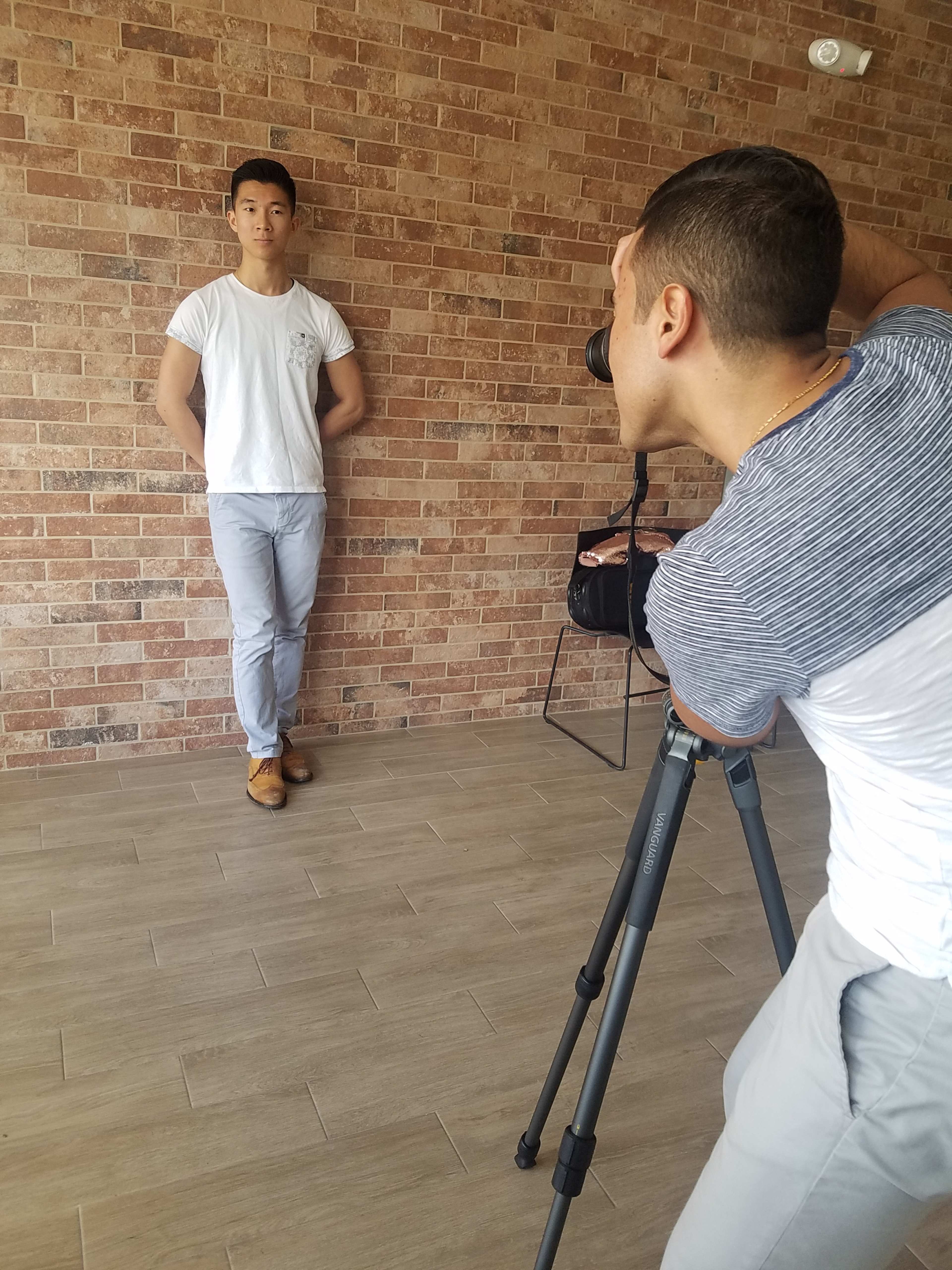 A photographer is capturing a portrait of a person standing against a brick wall.
