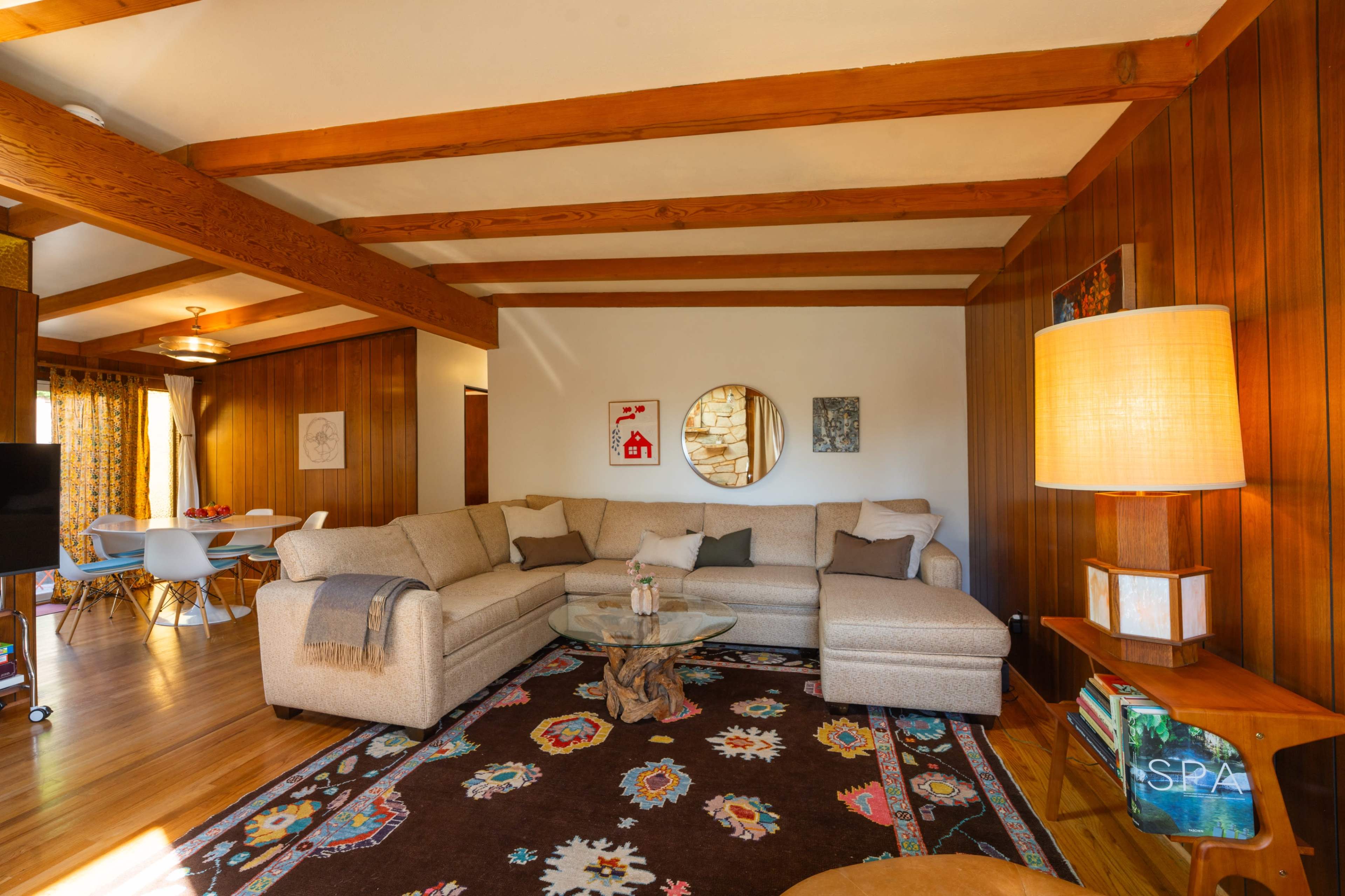 The living room features a sectional sofa, wooden beams on the ceiling, and a patterned area rug.