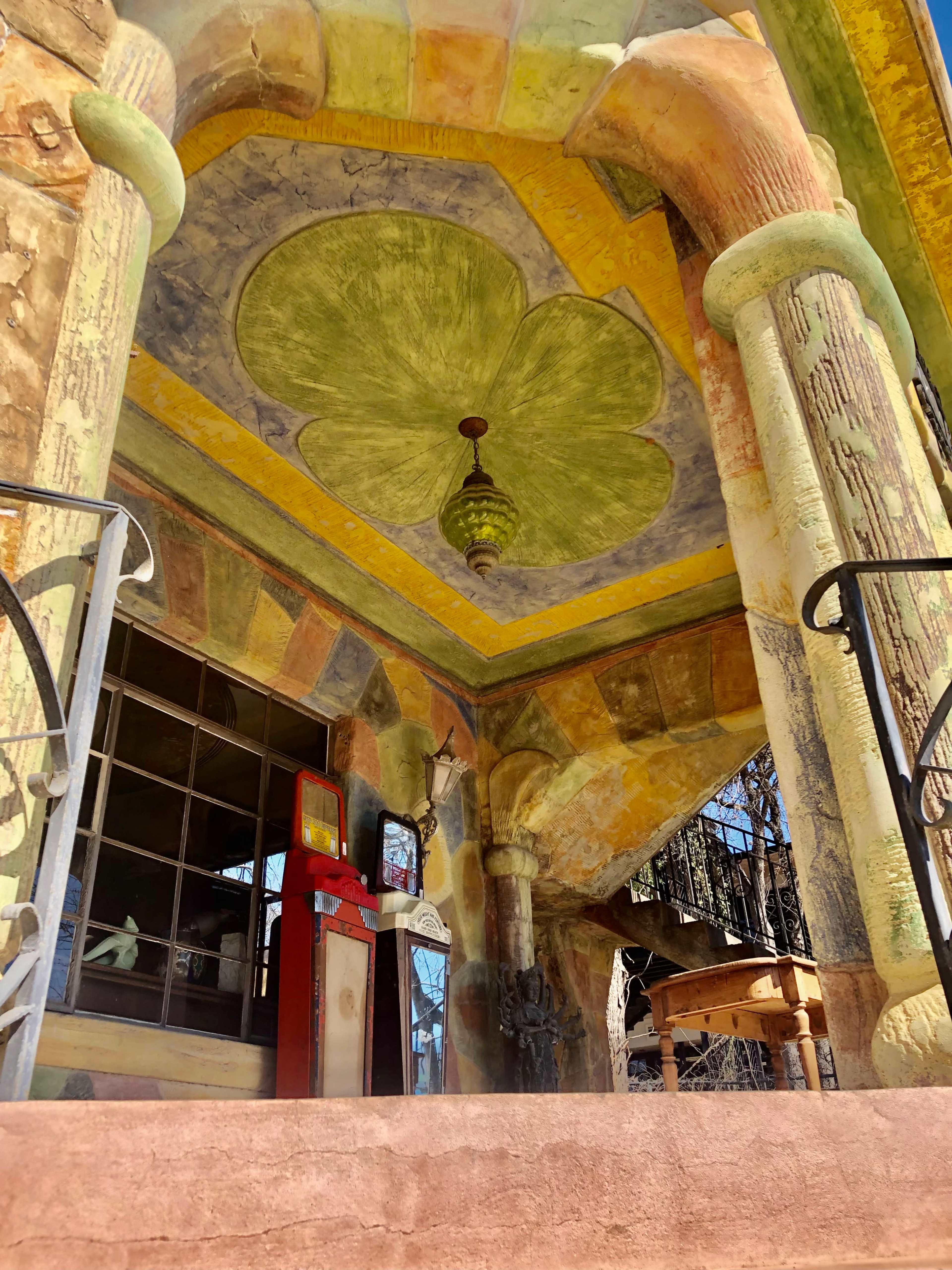 The image shows a vibrant, intricately designed entrance with colorful columns and a decorative ceiling, leading to a large window on the side.