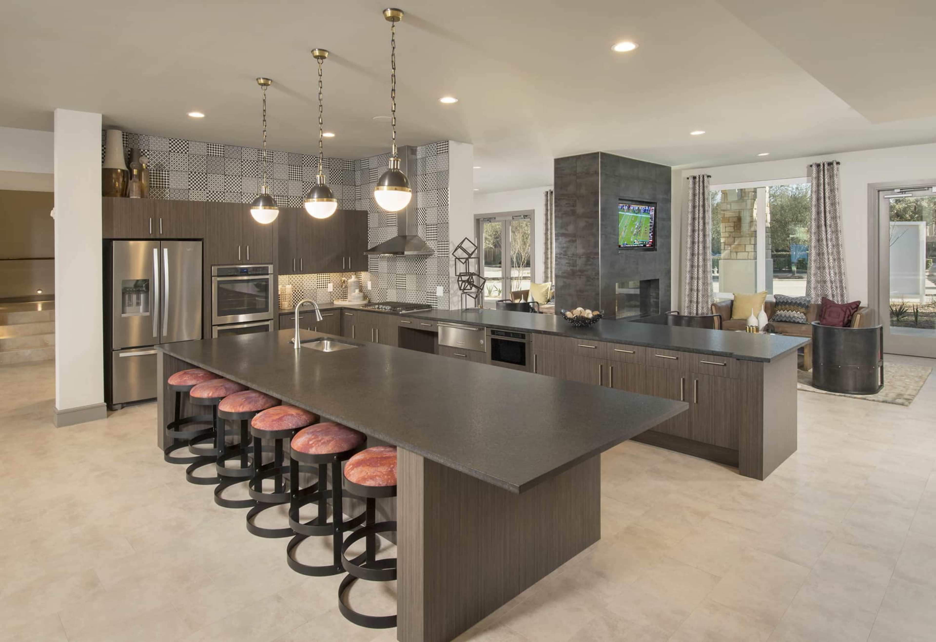 A modern kitchen with a large island, bar seating, stainless steel appliances, and a living area in the background.