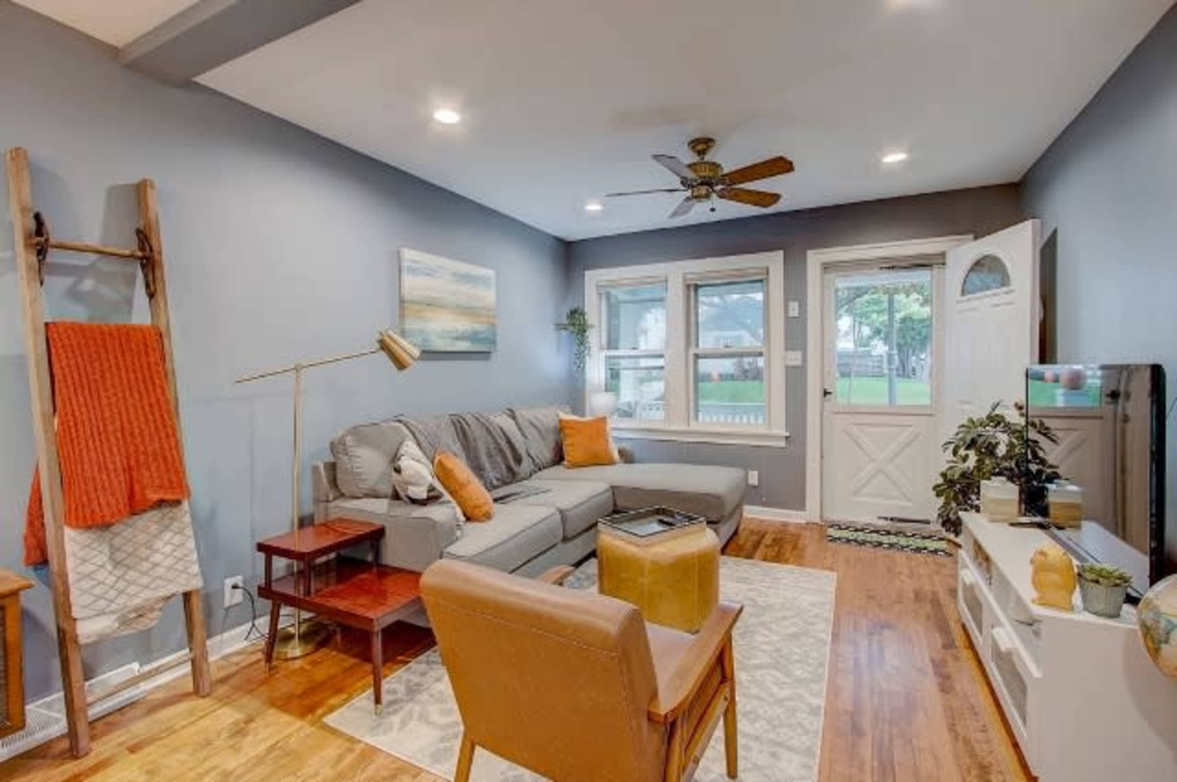 A living room with a gray sectional sofa, a wooden side table, an armchair, and large windows leading to an outdoor area.