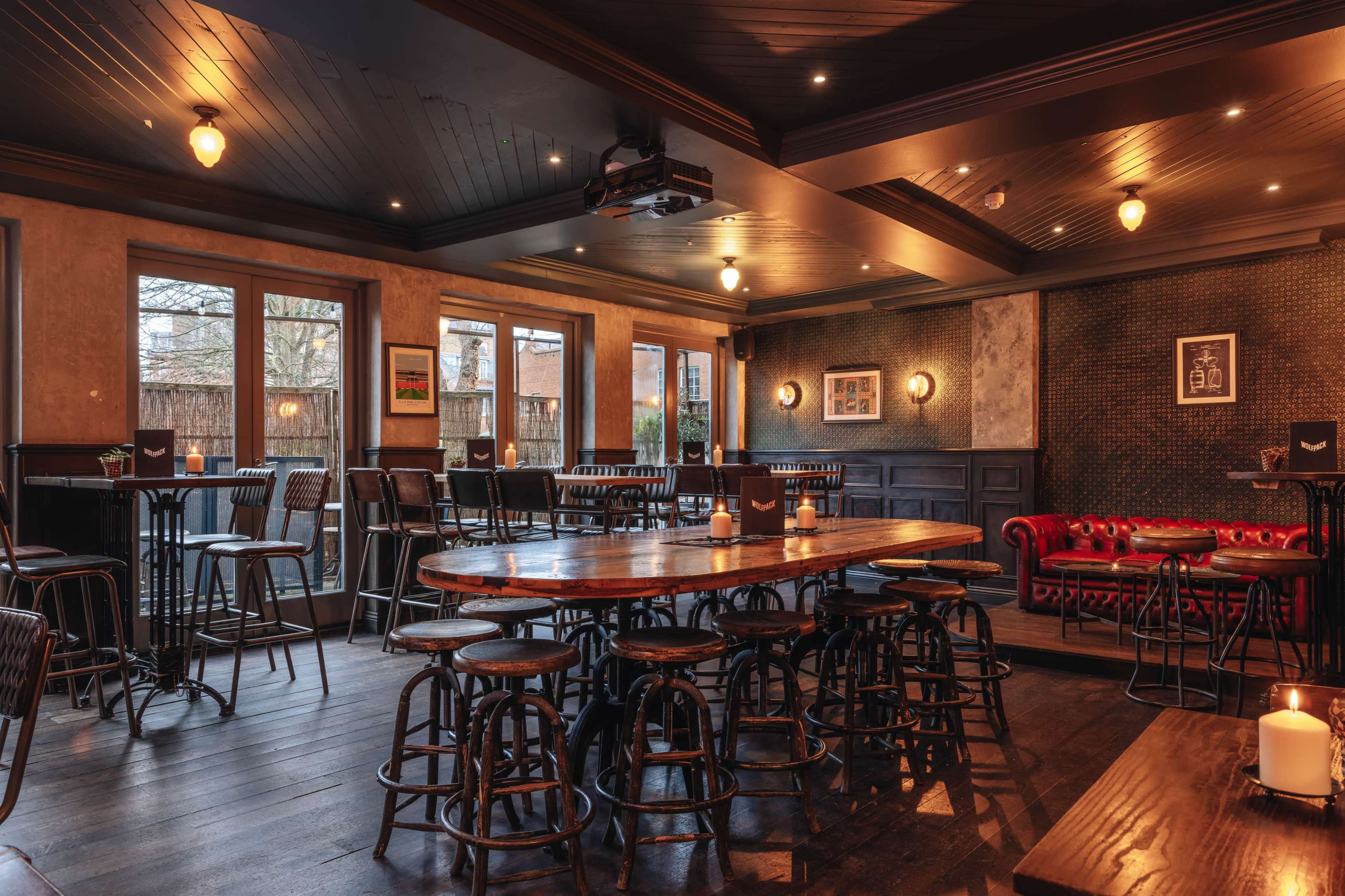 The image shows an interior of a bar with wooden tables, high chairs, and ambient lighting.