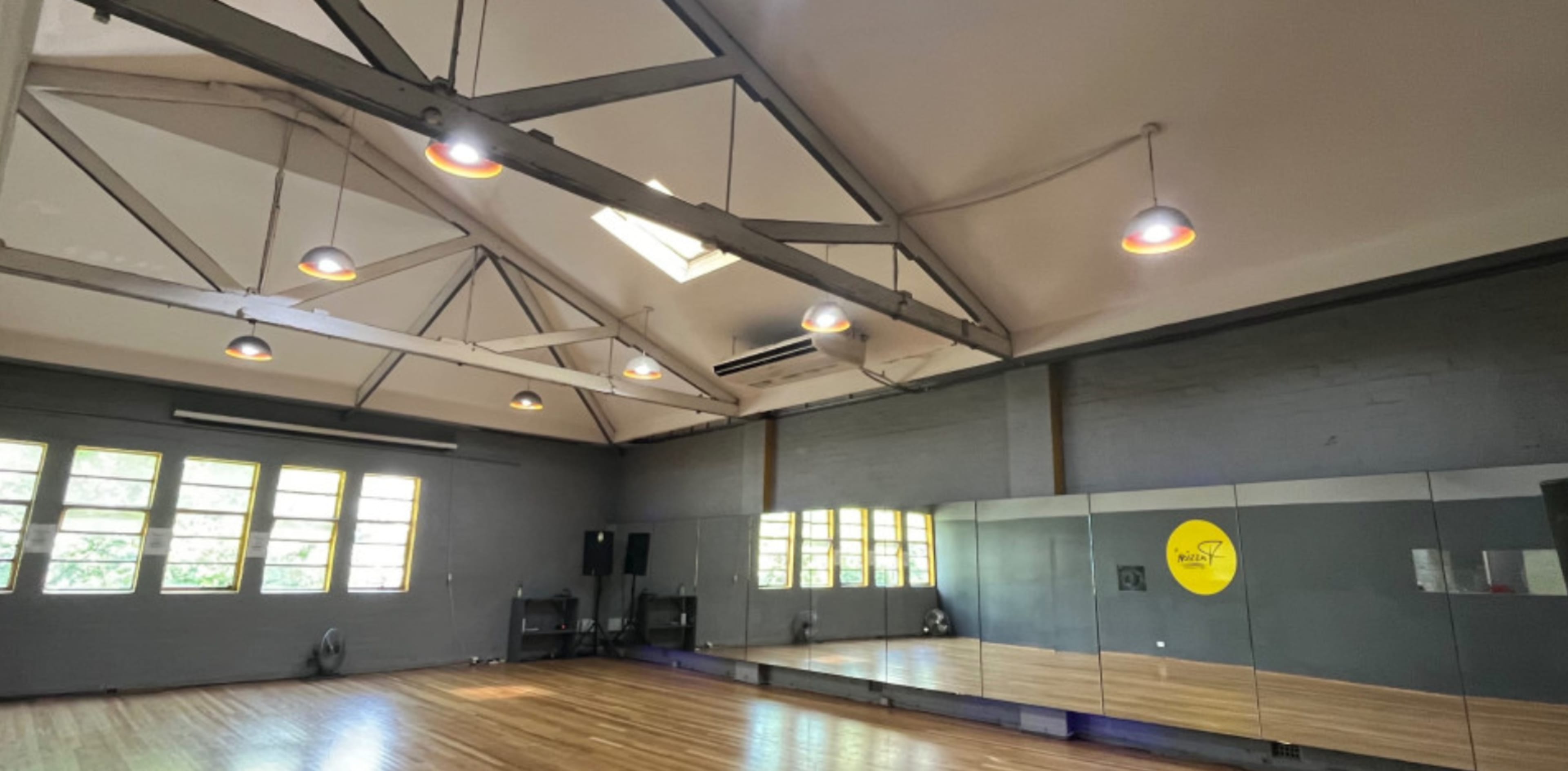 A bright studio space with high ceilings, large windows, and a mirrored wall.