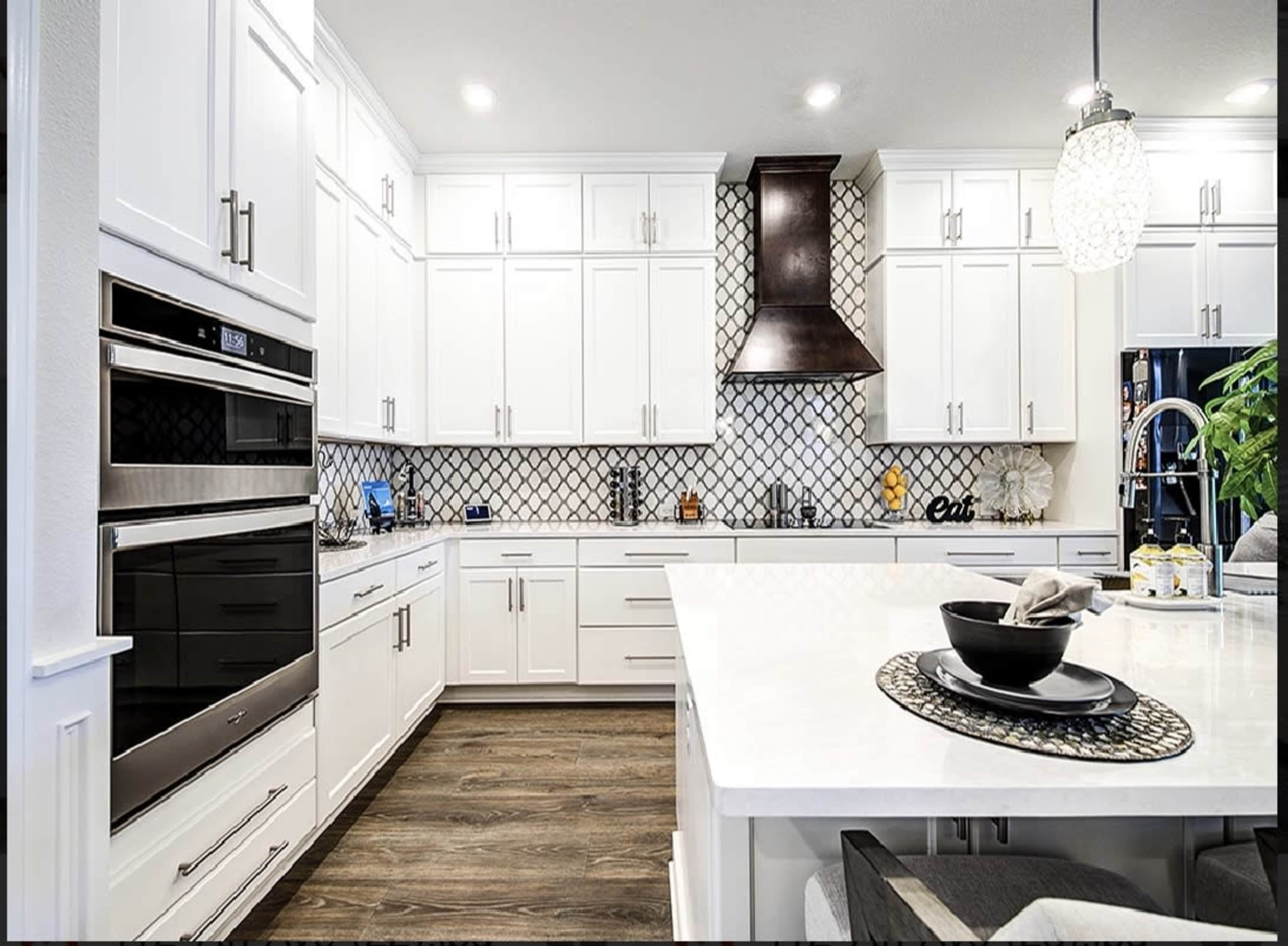 The kitchen features white cabinetry, a patterned backsplash, a stainless steel hood, and a central island with a black bowl on a decorative placemat.