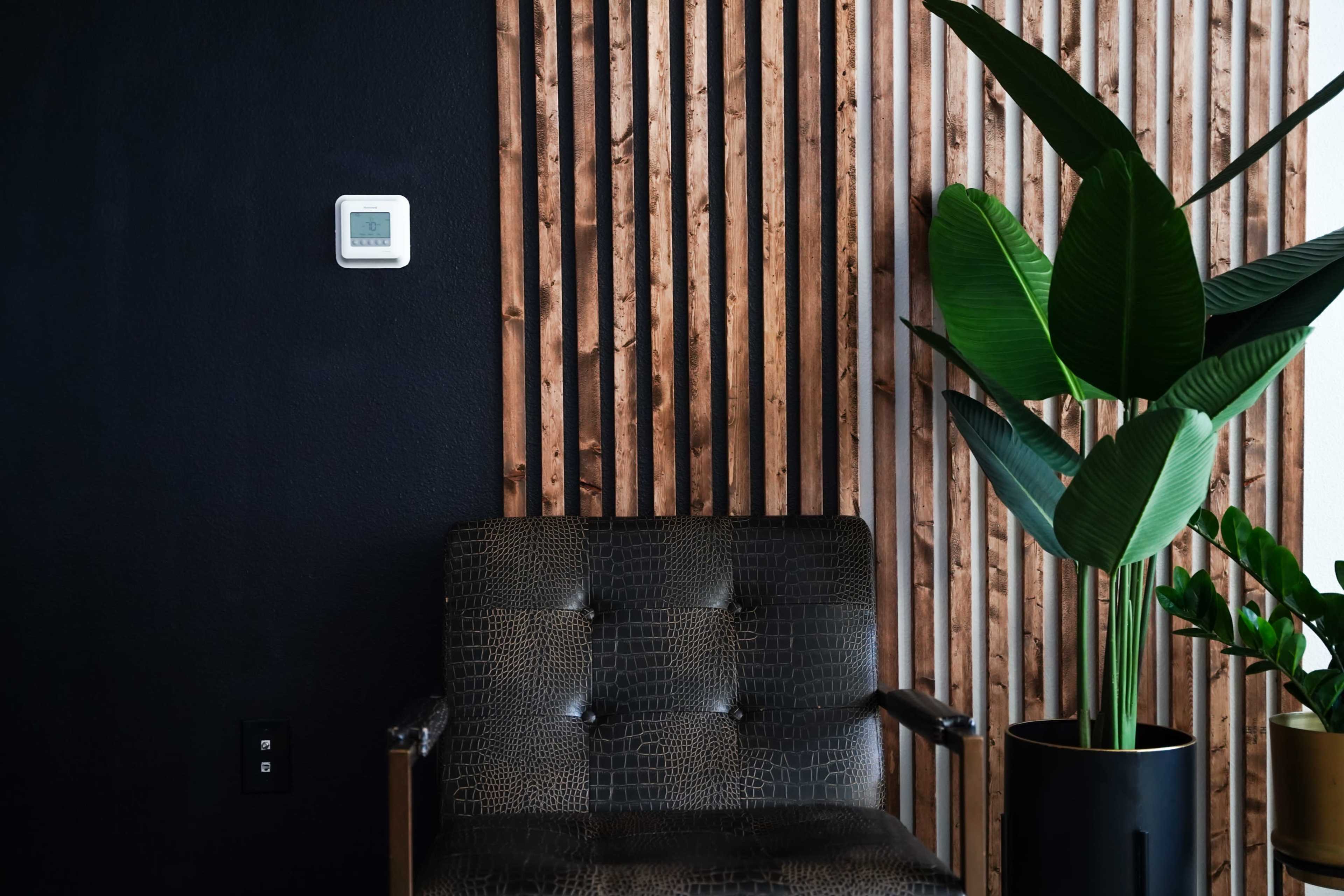 A black leather chair is positioned next to a wooden slat wall, with a green plant in a pot nearby.