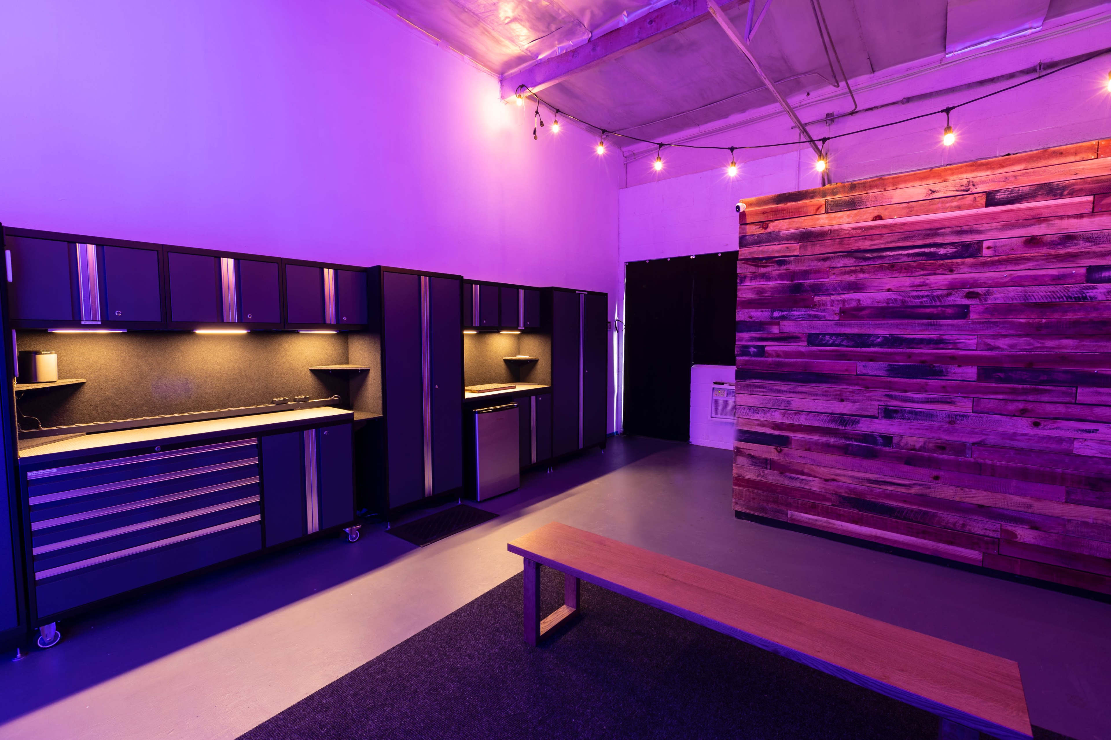 A modern interior space features purple lighting, a wooden accent wall, a wooden bench, and cabinetry along one side.