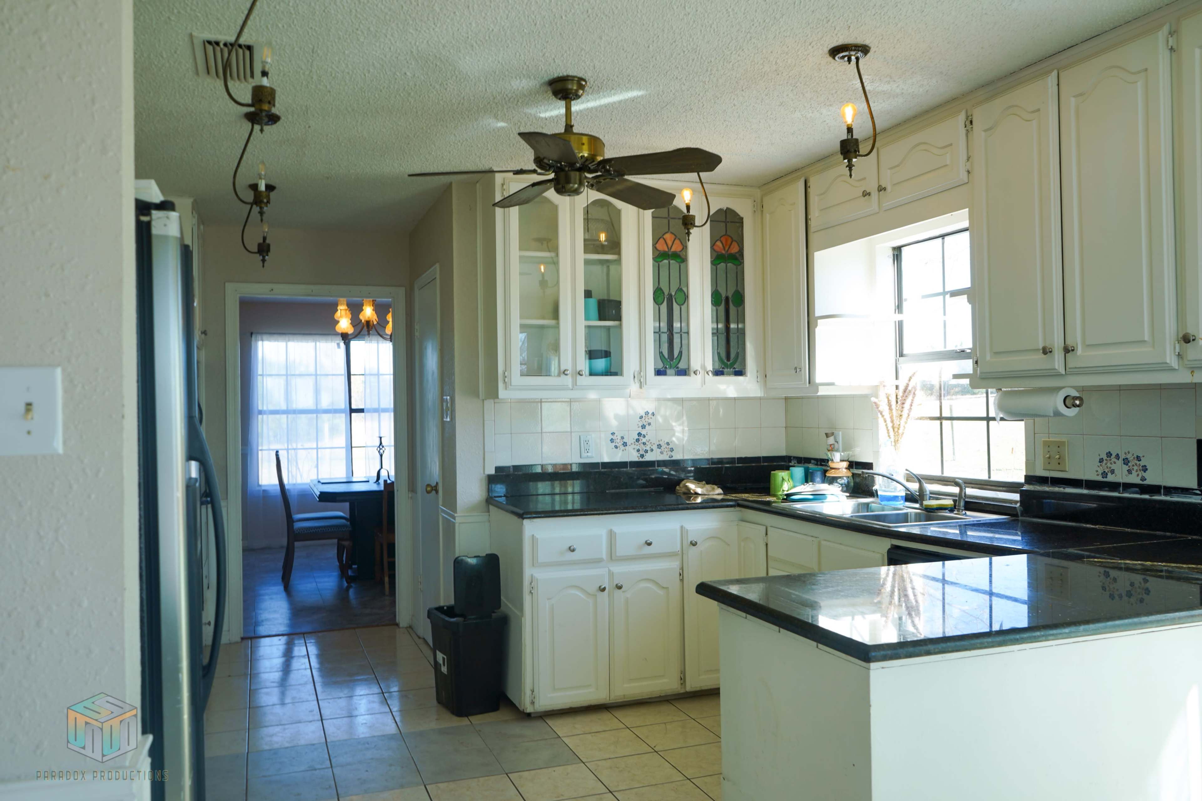 A well-lit kitchen with white cabinets, black countertops, and a window overlooking a dining area.