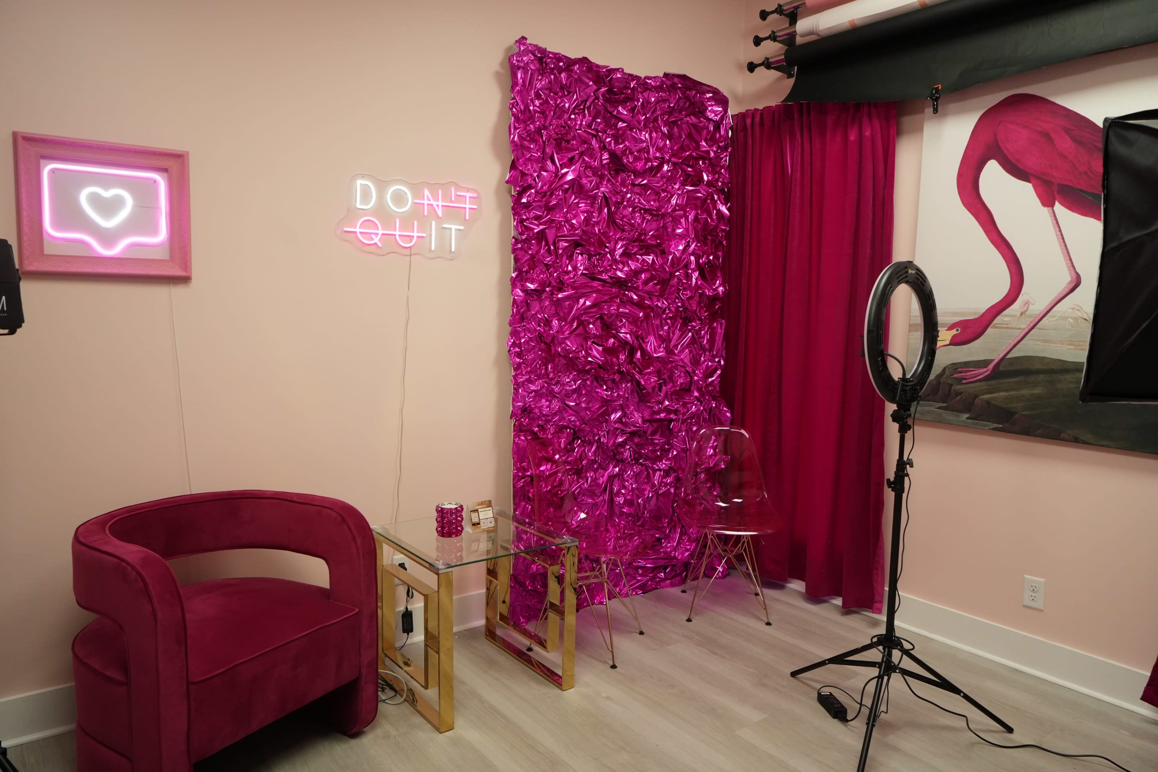 The scene features a small photography studio with a pink-themed backdrop, a plush chair, and neon signs.