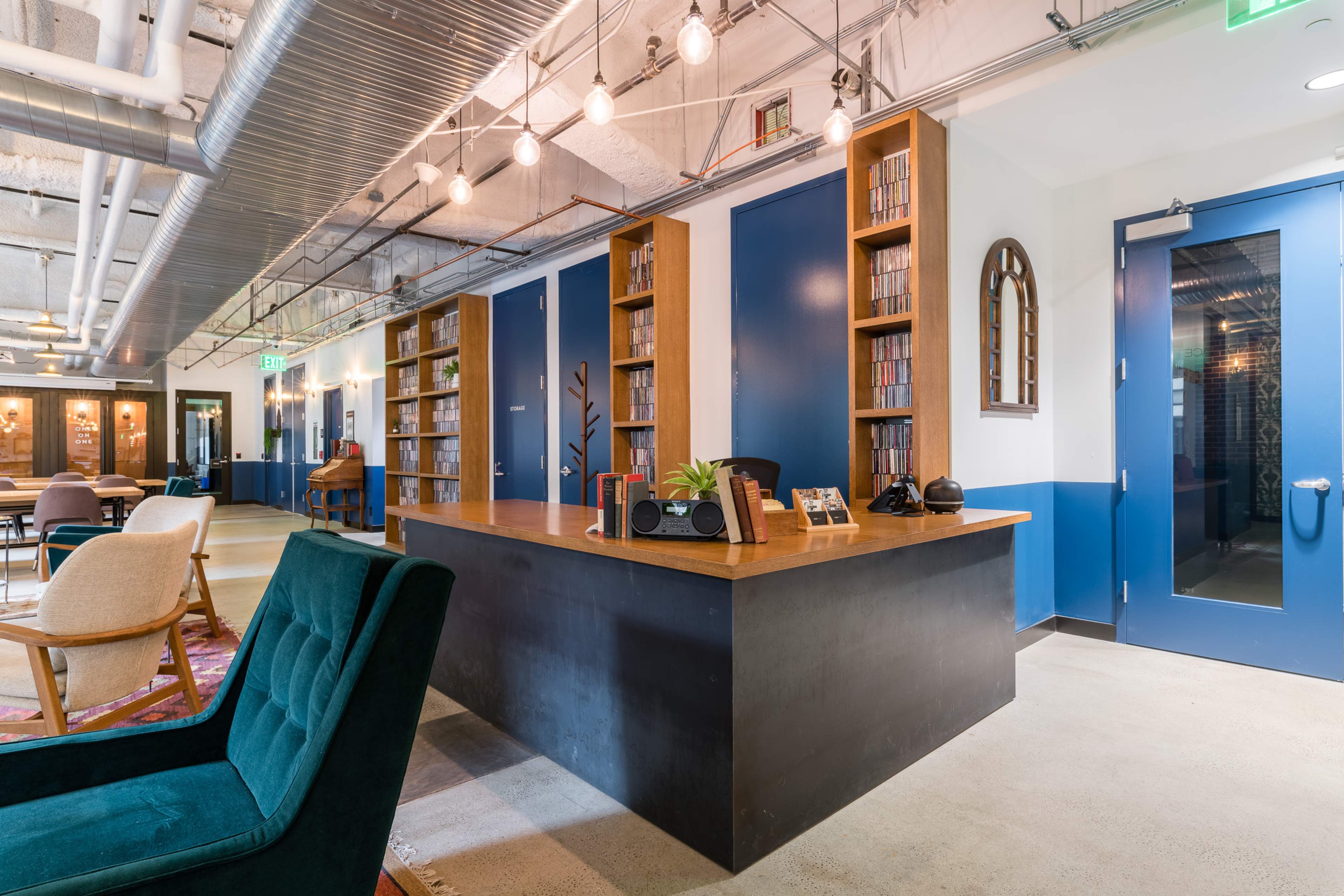 A modern office space features a reception area with wooden bookshelves, a wooden desk, and various seating options.