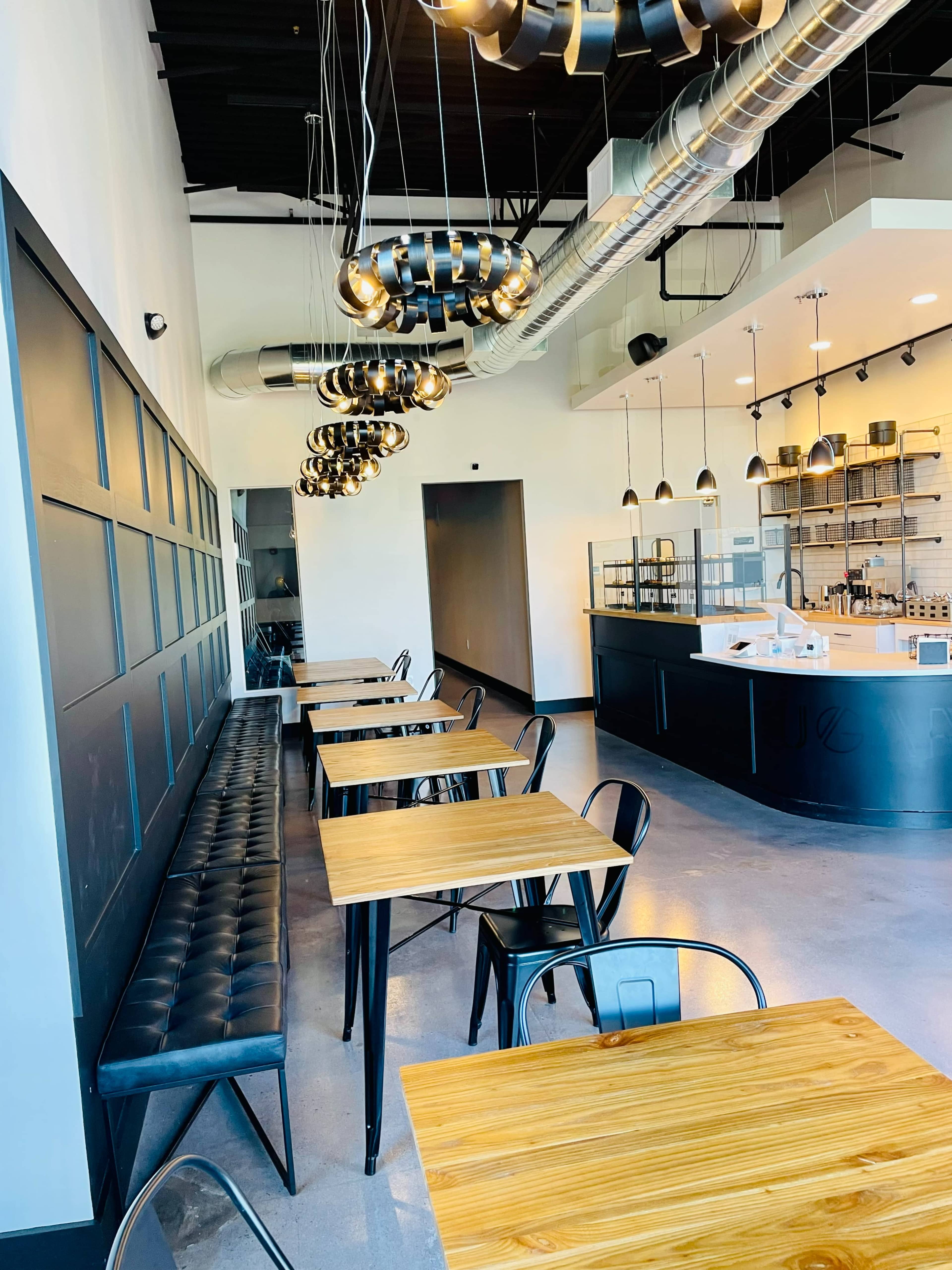 A modern café interior featuring black seating along the walls, wooden tables, and industrial-style lighting fixtures.