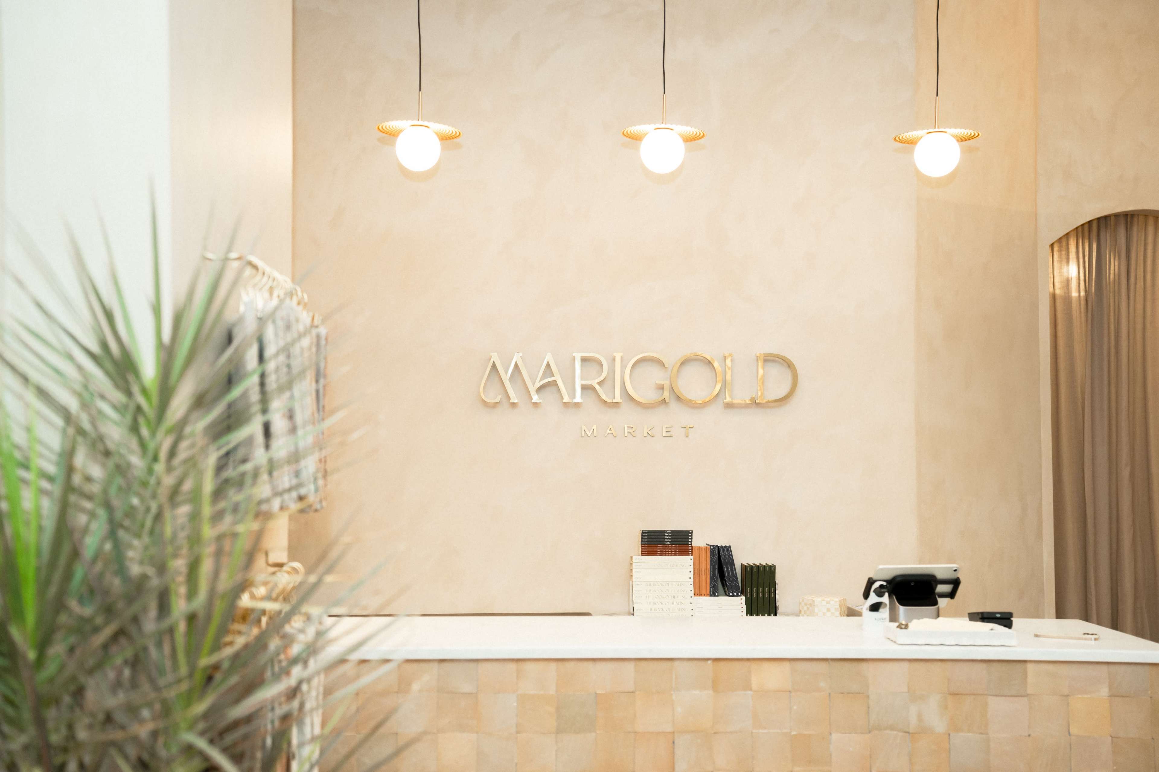 A minimalist reception area features a light-colored wall with the "MARIGOLD MARKET" sign above a tidy white counter and modern lighting fixtures.