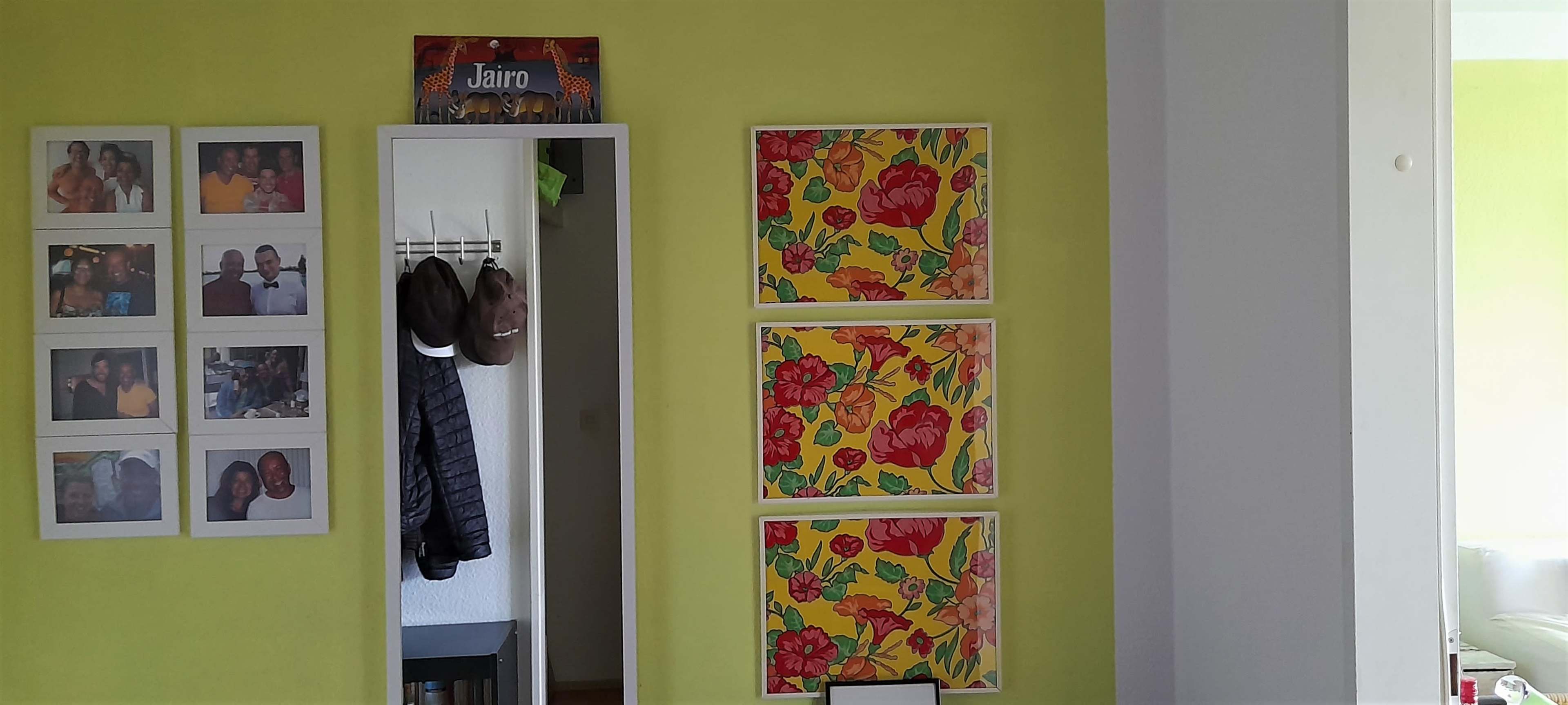 The image shows a brightly colored room with framed photos on the wall, a mirror, and decorative floral artwork.