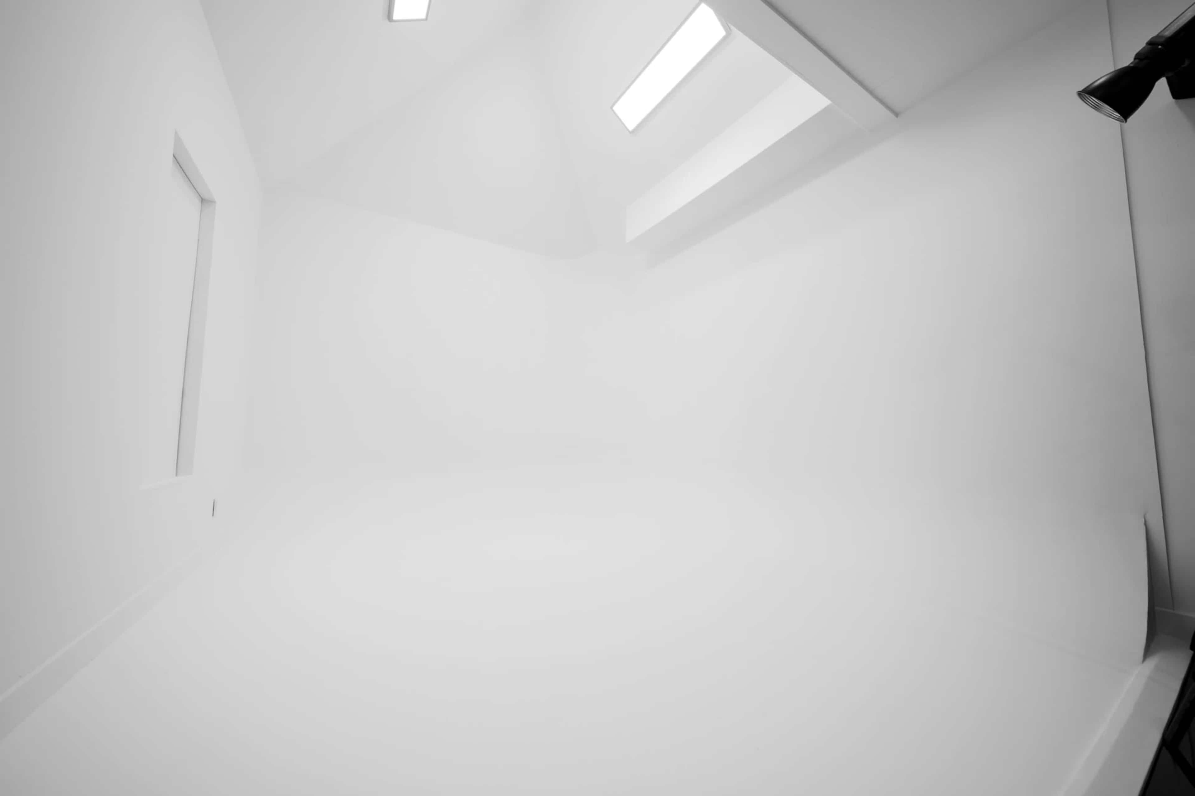 A minimalistic white interior space with a sloped ceiling and a single light source.