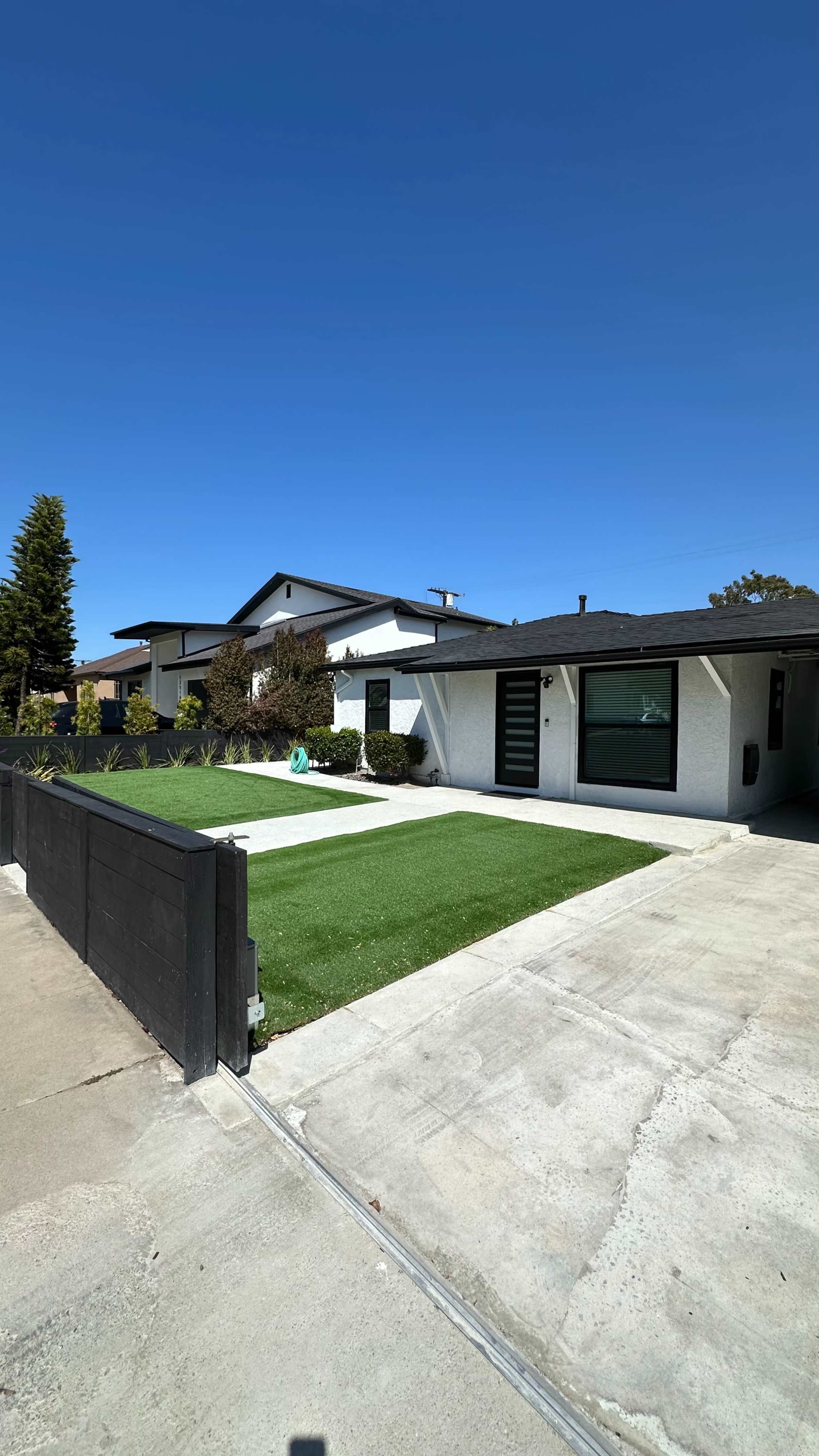 The image shows a modern residential property with a manicured lawn and a concrete driveway, featuring two distinct architectural styles in the background.