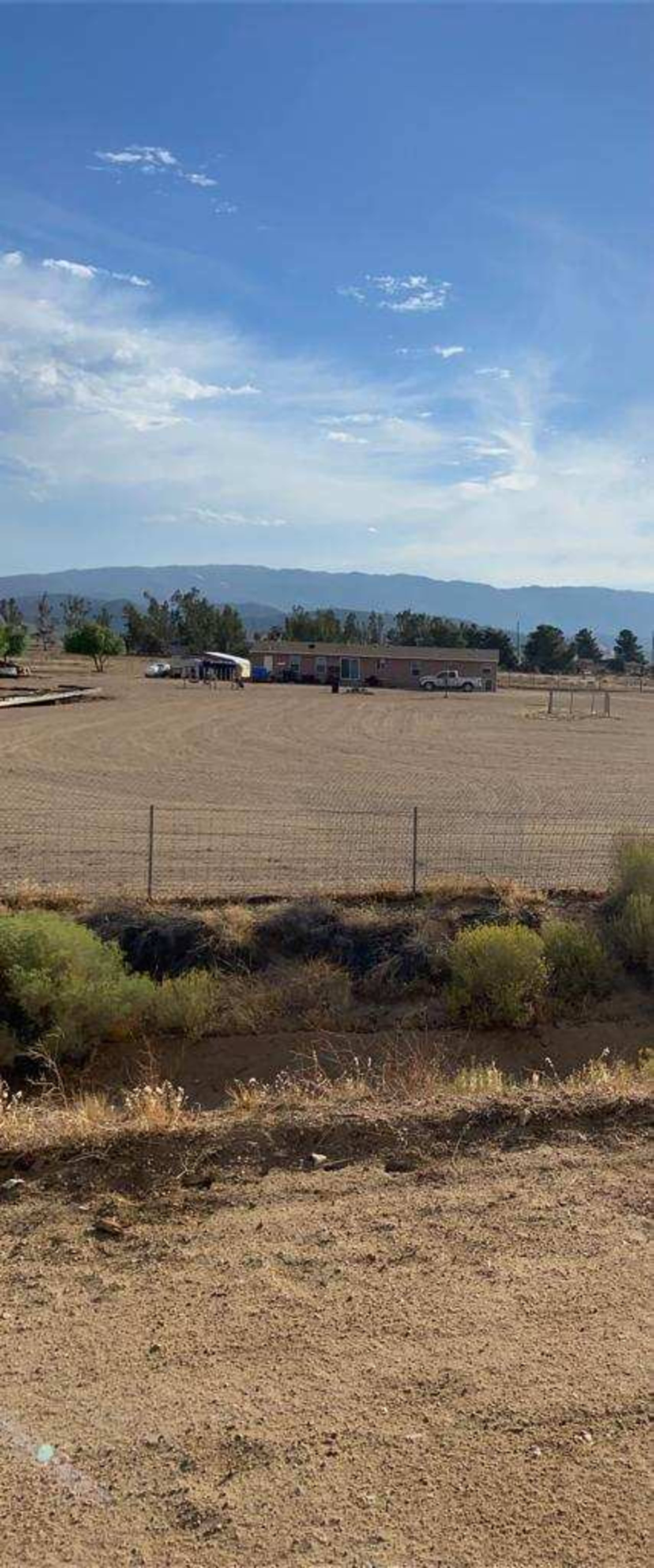 The image shows a flat, open field with a distant building surrounded by sparse vegetation and mountains in the background.