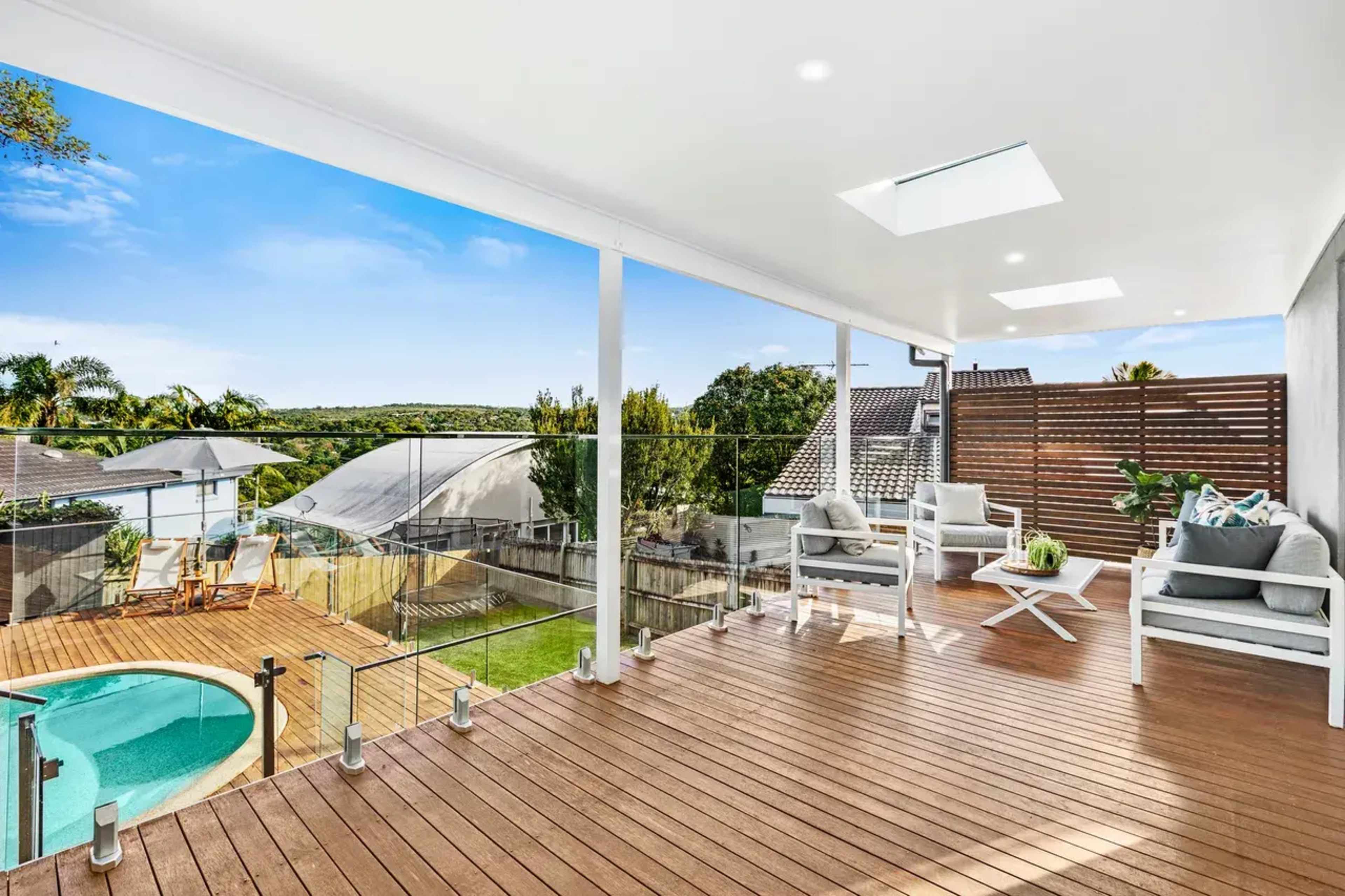 A modern outdoor deck with a clear view of a swimming pool and landscaped yard, featuring glass railings and comfortable seating.