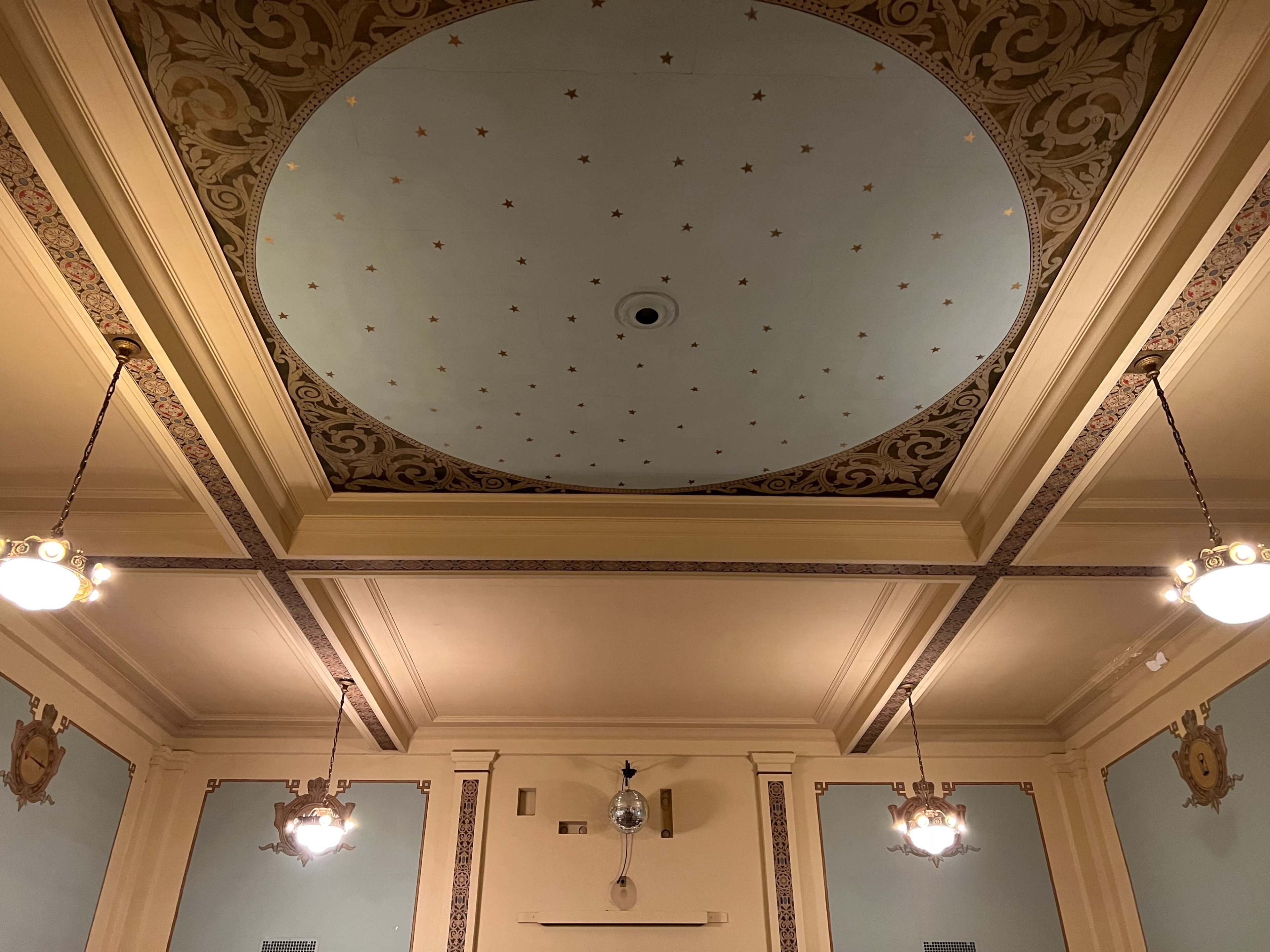 An elaborately decorated ceiling with a central circular design, surrounded by ornate molding and flanked by ornate light fixtures.