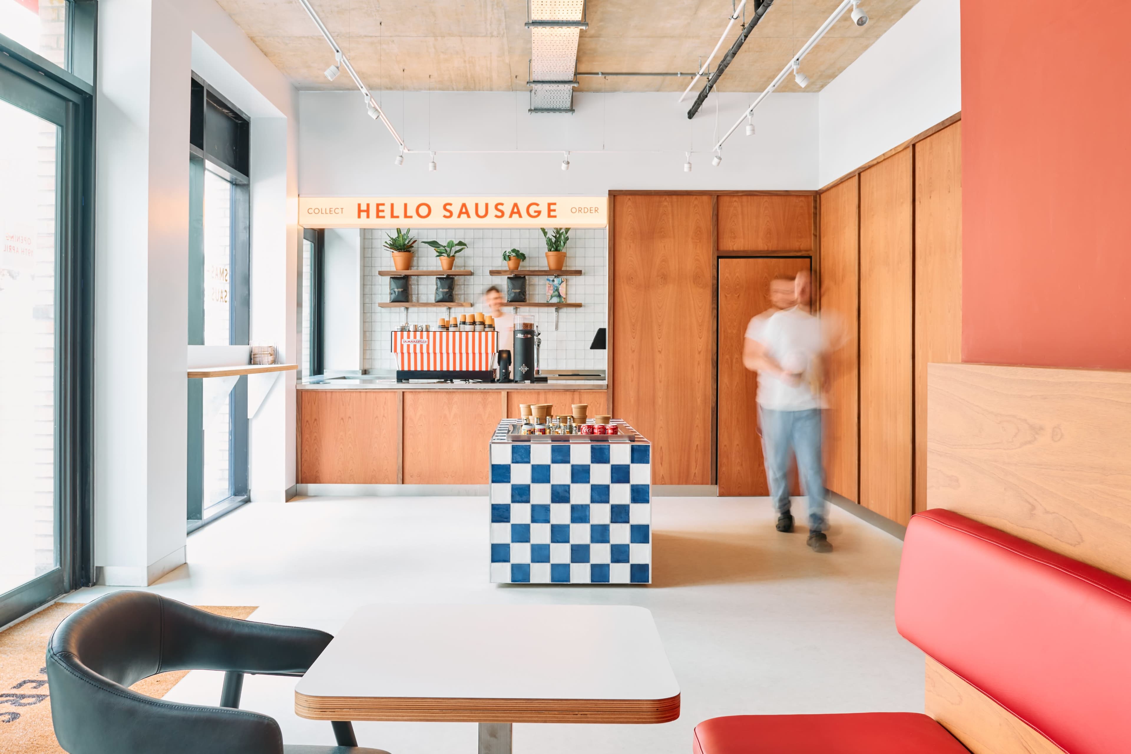 A modern food counter with wooden walls, a checkered blue and white service area, and a person walking in a casual dining space.
