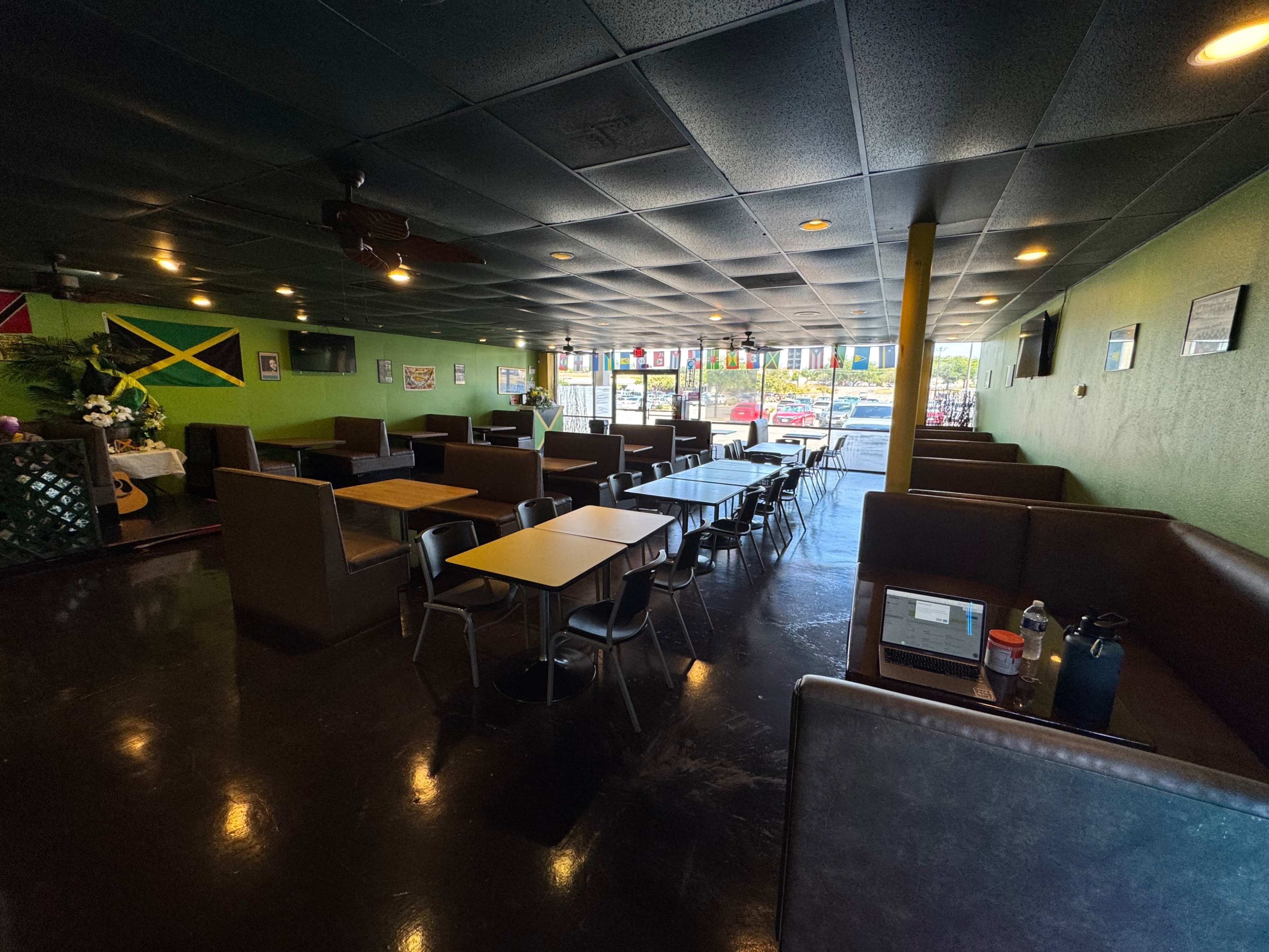 The image shows a spacious restaurant interior with multiple tables and booths, decorated with Jamaican flags and featuring large windows.