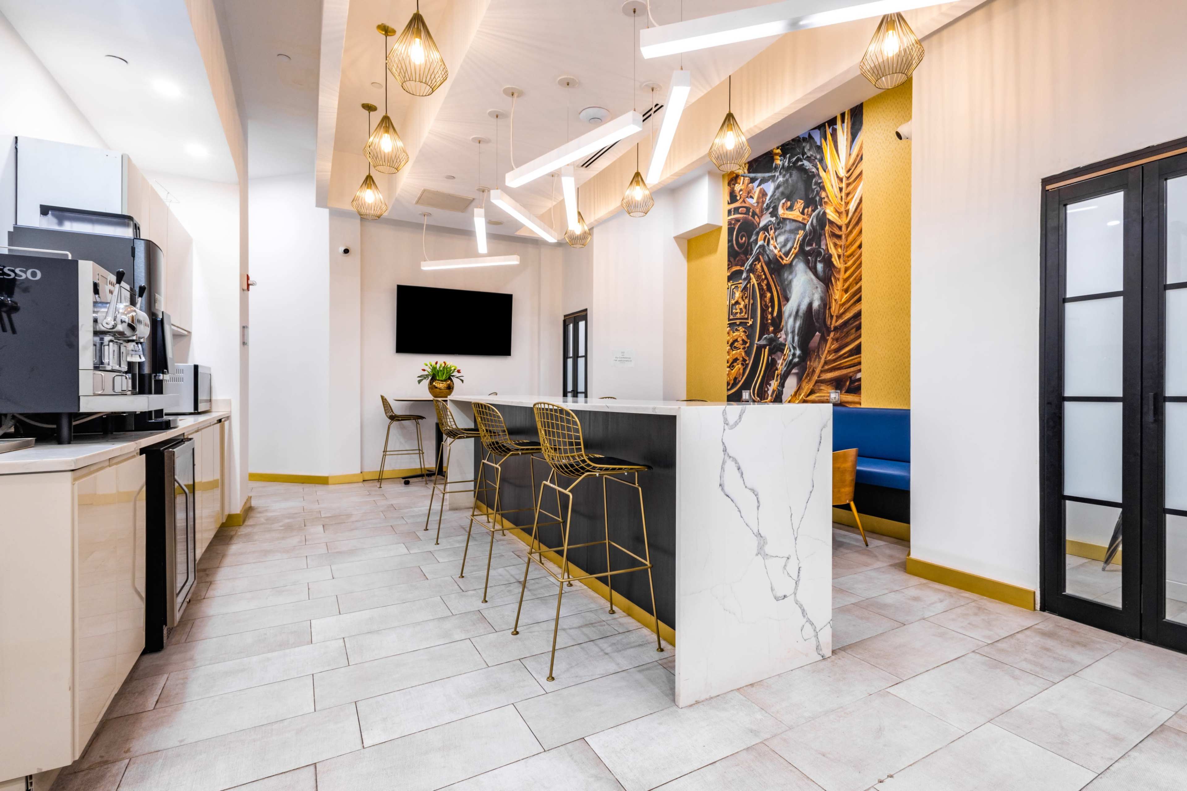 The image shows a modern kitchen or lounge area featuring a coffee station, high chairs at a bar-style table, and a large wall decoration with a horse portrait.