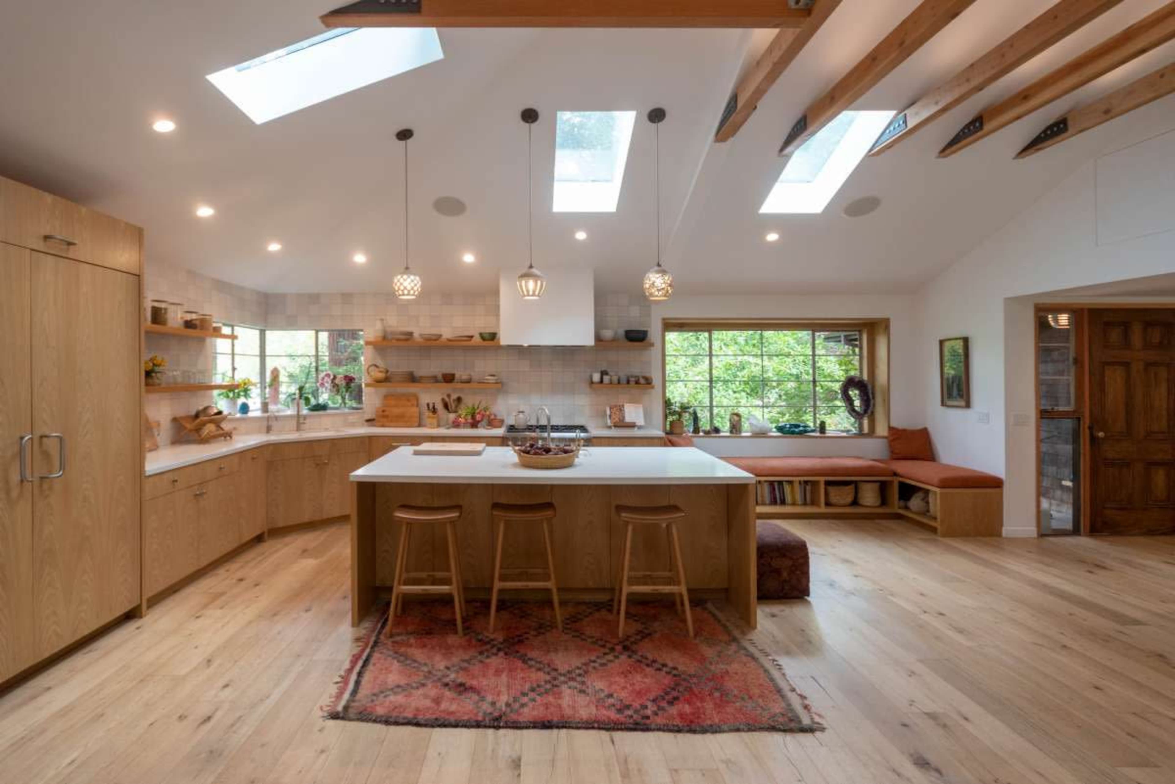 A modern kitchen with wooden cabinetry, a large island with three stools, and skylights above, creating a bright and inviting space.